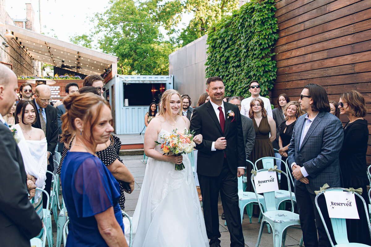 A bride walks with her father down the aisle for her outdoor ceremony at The Joinery in Chicago