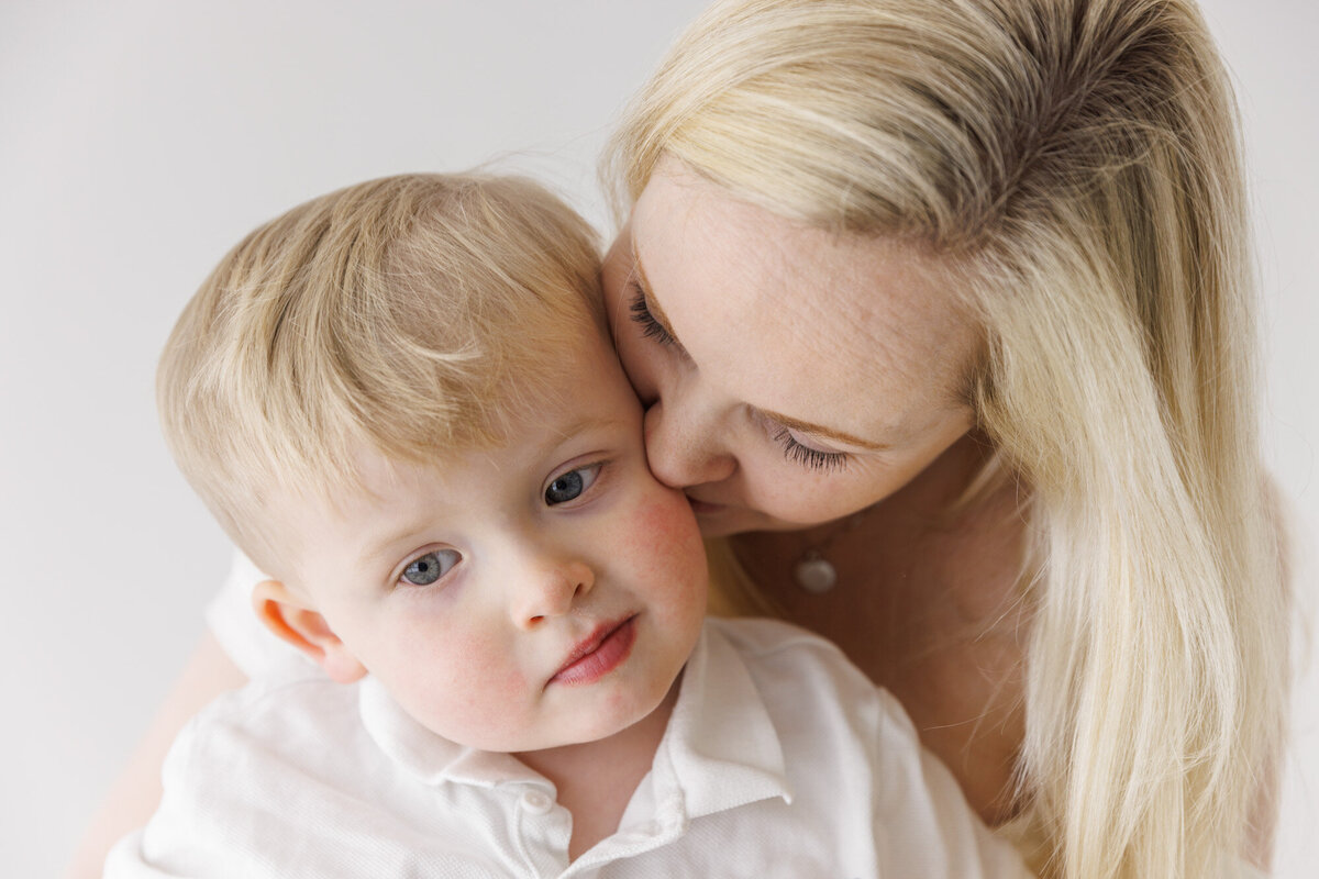 En mor kysser sønnen sin på kinnet, hun står bak ham. Nærbilde av ansiktene deres. Fotografert i Studio Landmark, Fyllingsdalen.