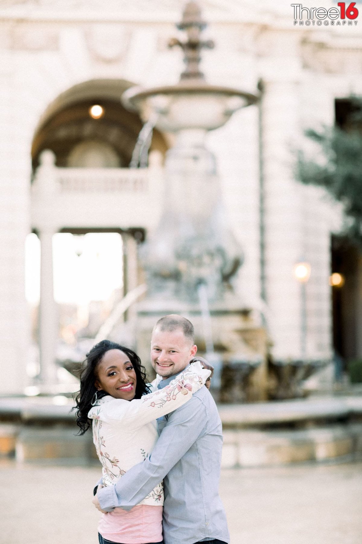 Engaged couple give each other a big hug in front of the Pasadena City Hall water fountain