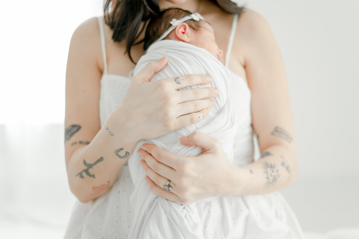 A woman with tattoos on her arms holds her newborn baby In Kristie Lloyd’s Nashville newborn photographer studio