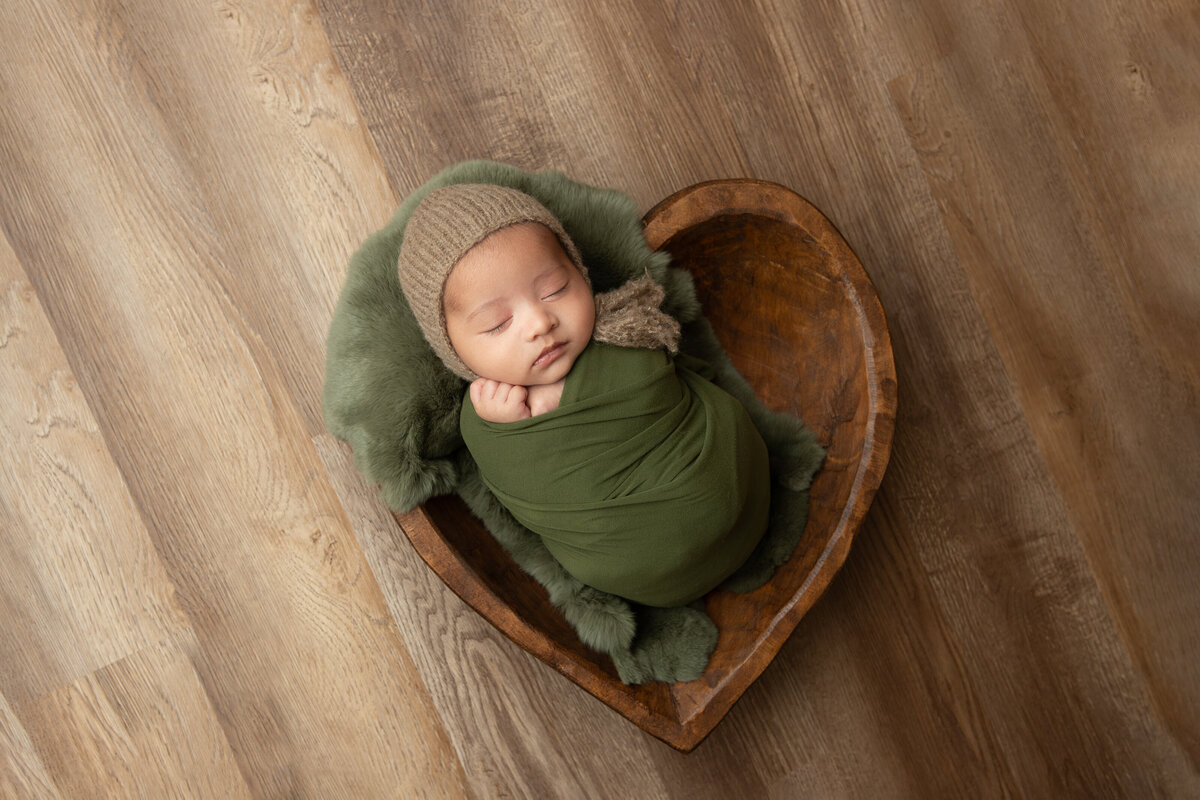 Olive green wrapped newborn in a rabbit fur stuffed carved wooden heart bowl