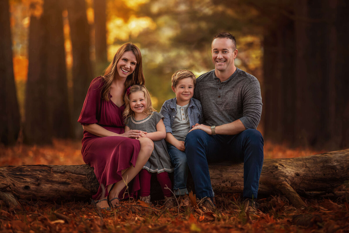 Family sitting outside on log with fall background