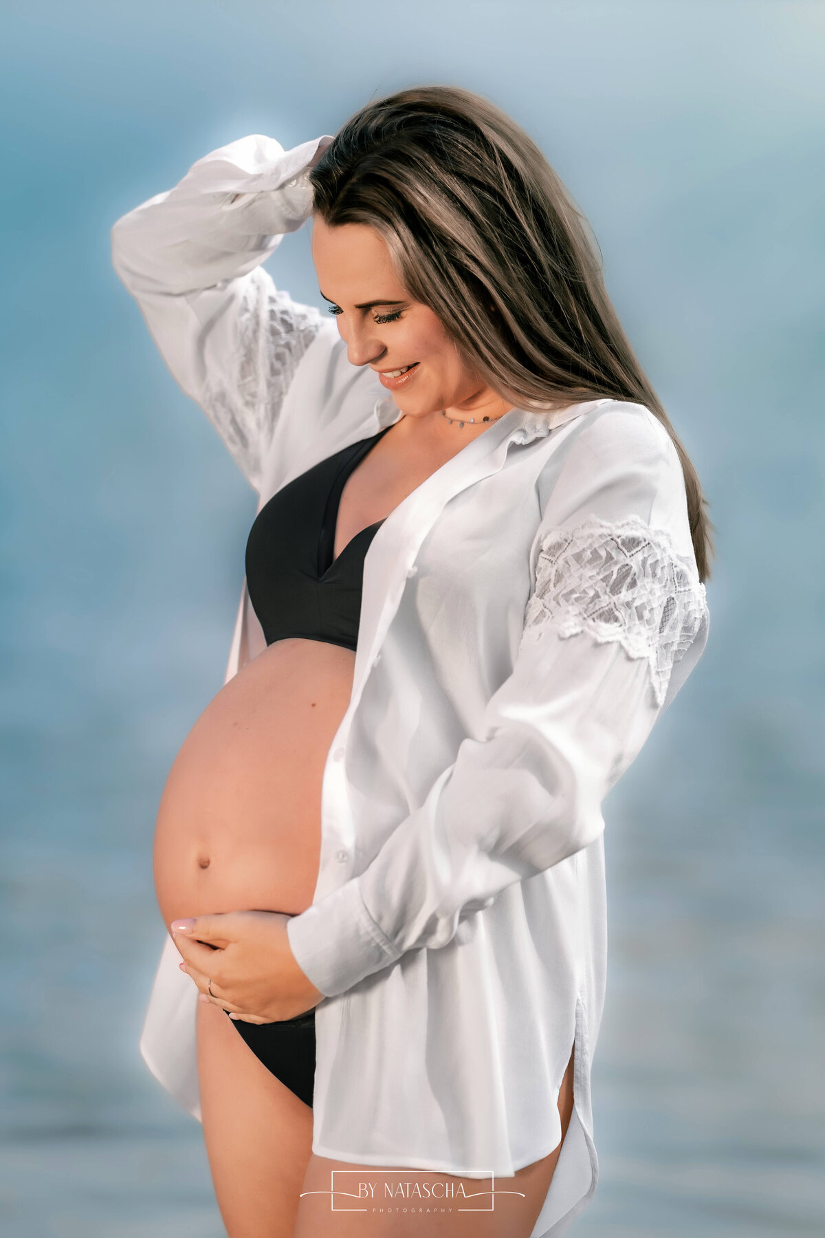 Zwangere vrouw in zwarte lingerie met witte blouse en helder water op de achtergrond