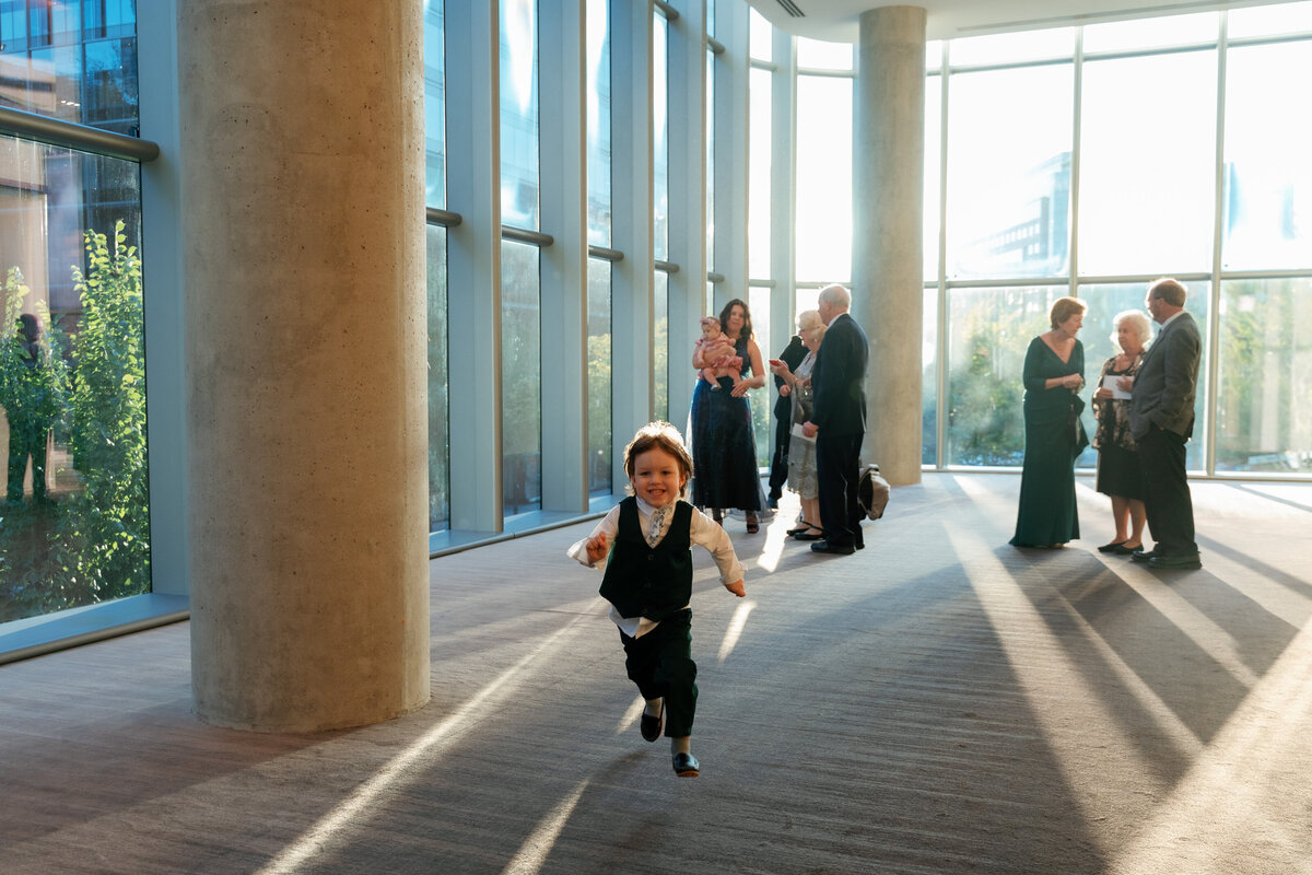 a little boy who is a guest at a wedding is running towards the photography and probably going to someone behind him. 