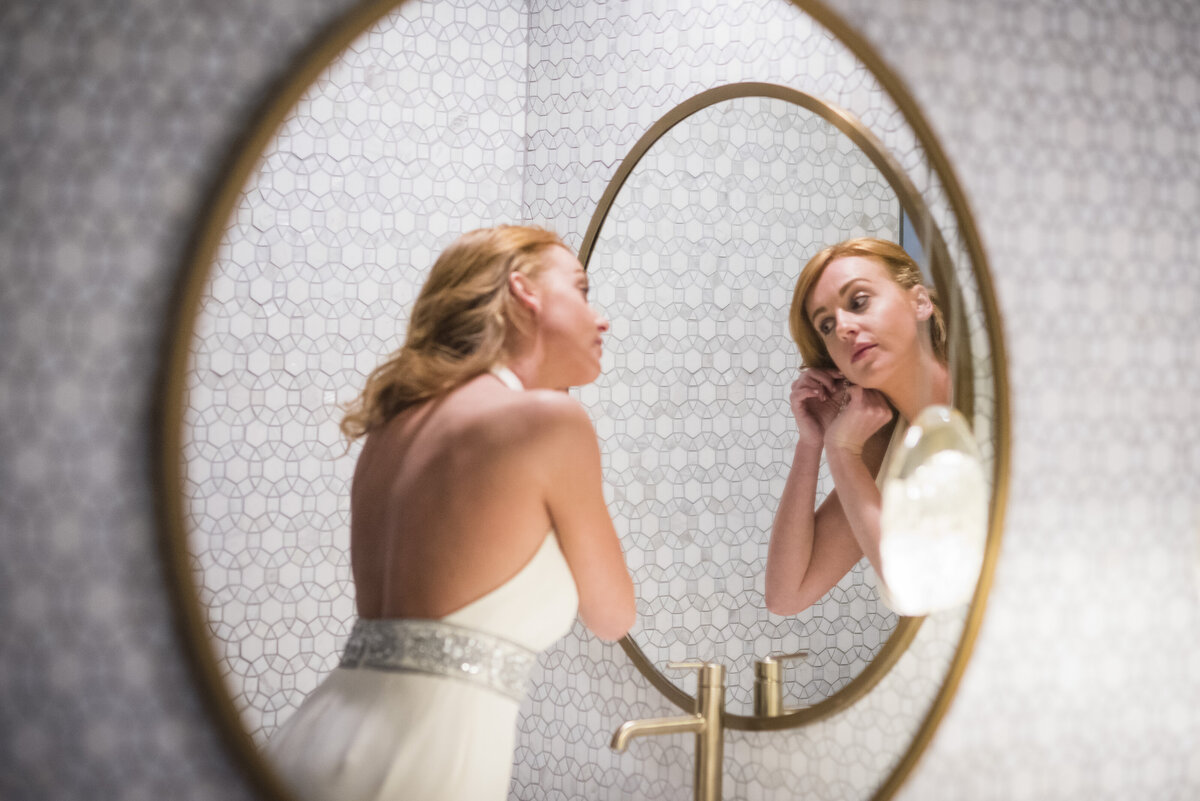 A bride looks in an oval mirror as she puts in her earring.