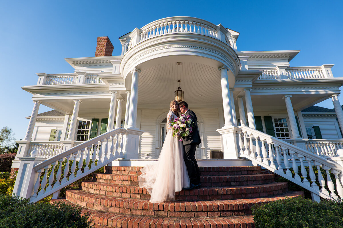 A wedding couple standing close together on a staircase leading to a house 