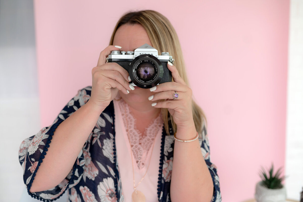 Photographer, Trysh Jaeger, takes a photo in front of pink backdrop
