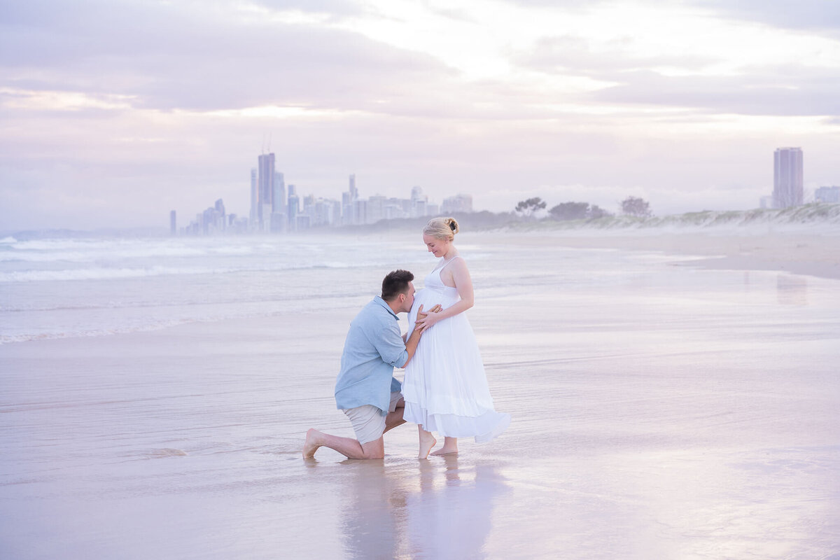couple kissing during maternity photo session in gold coast against gold coast skyscrapers city skyline
