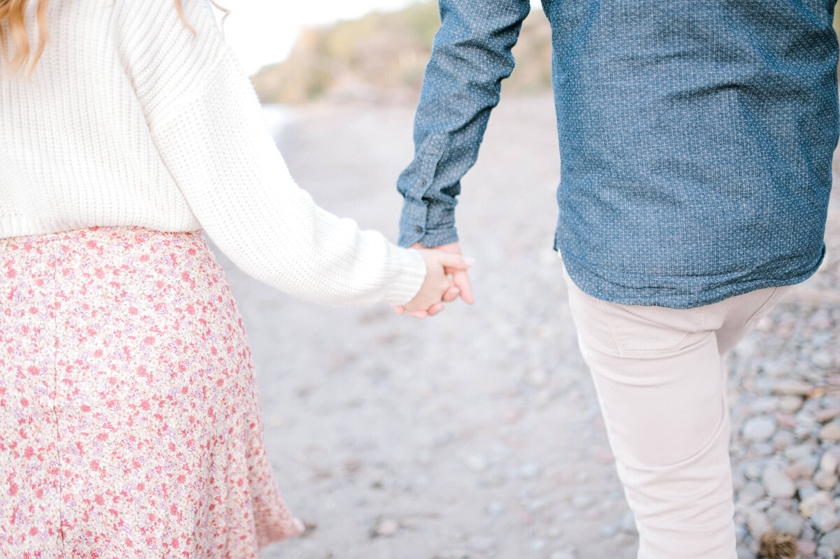 Man and woman hold hands while walking down the beach