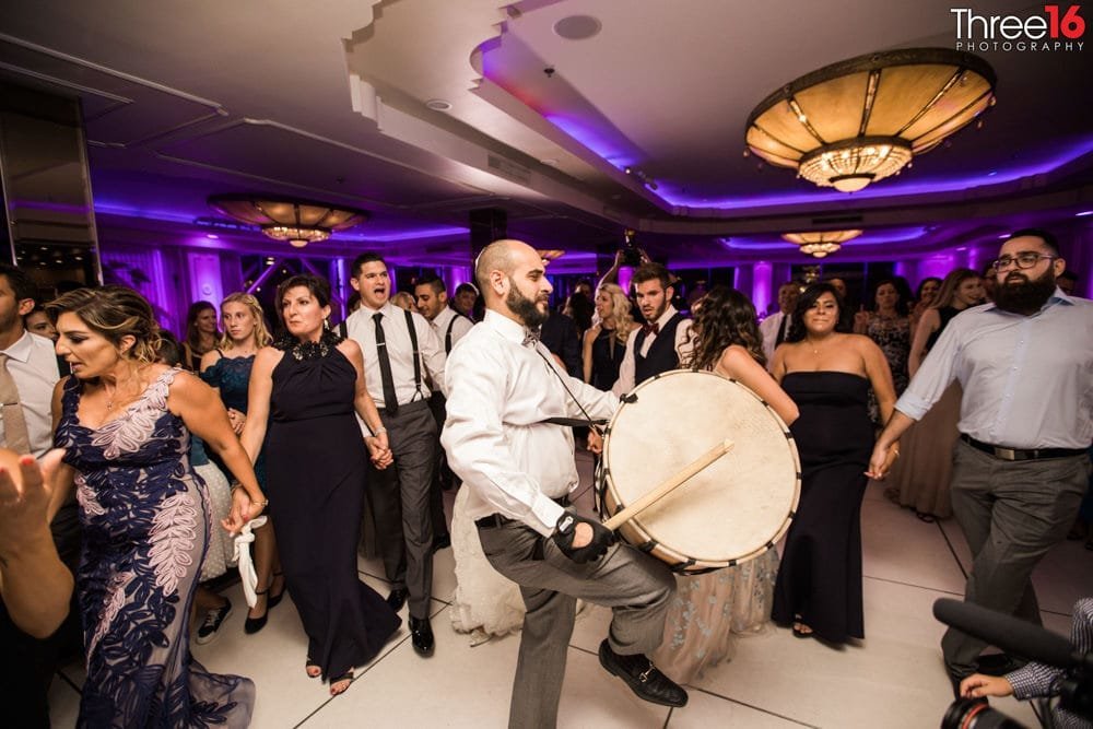 Wedding guests beating a drum on the dance floor while other dance