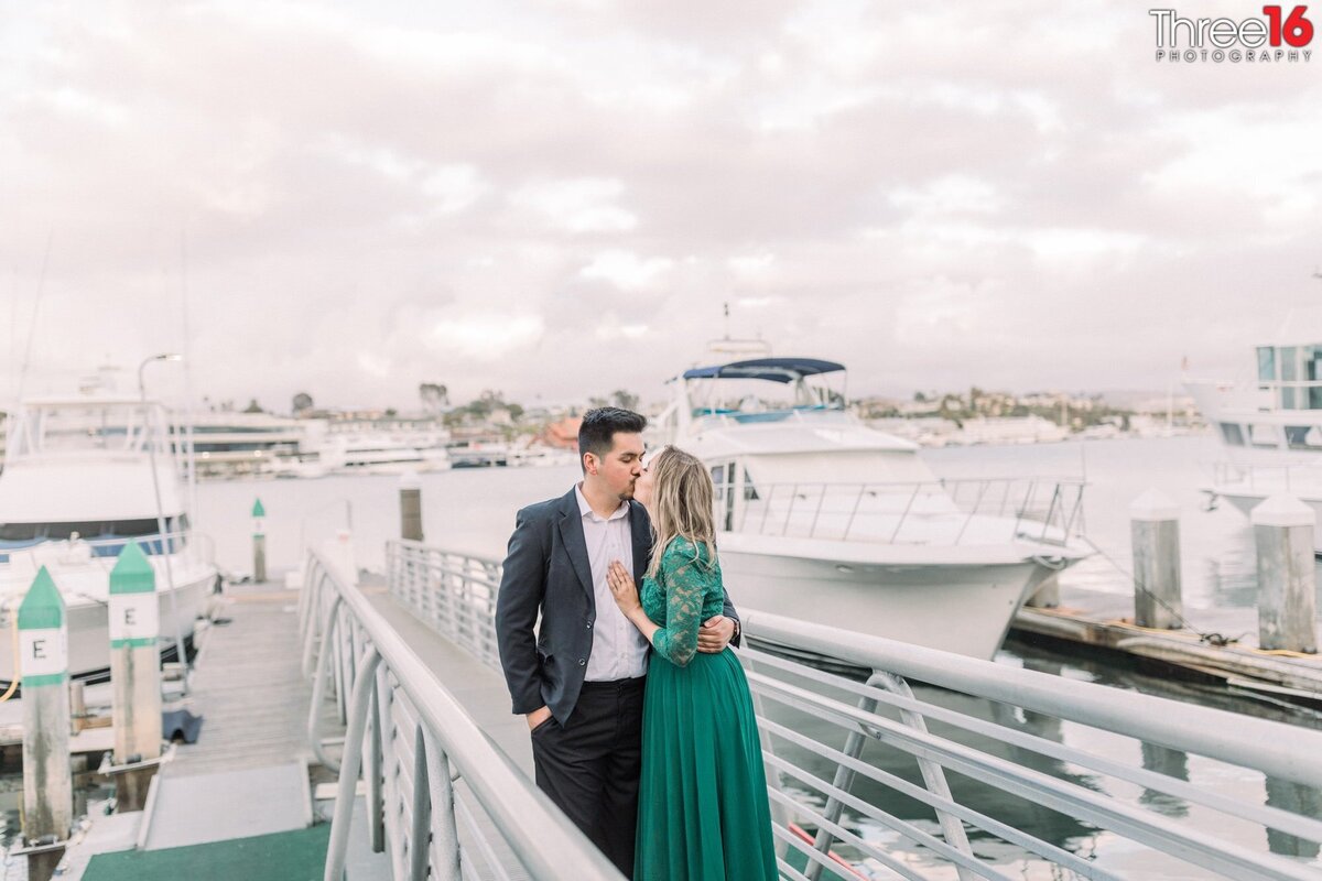 Engaged couple share a kiss while standing on the harbor docks at Lido Marina Village