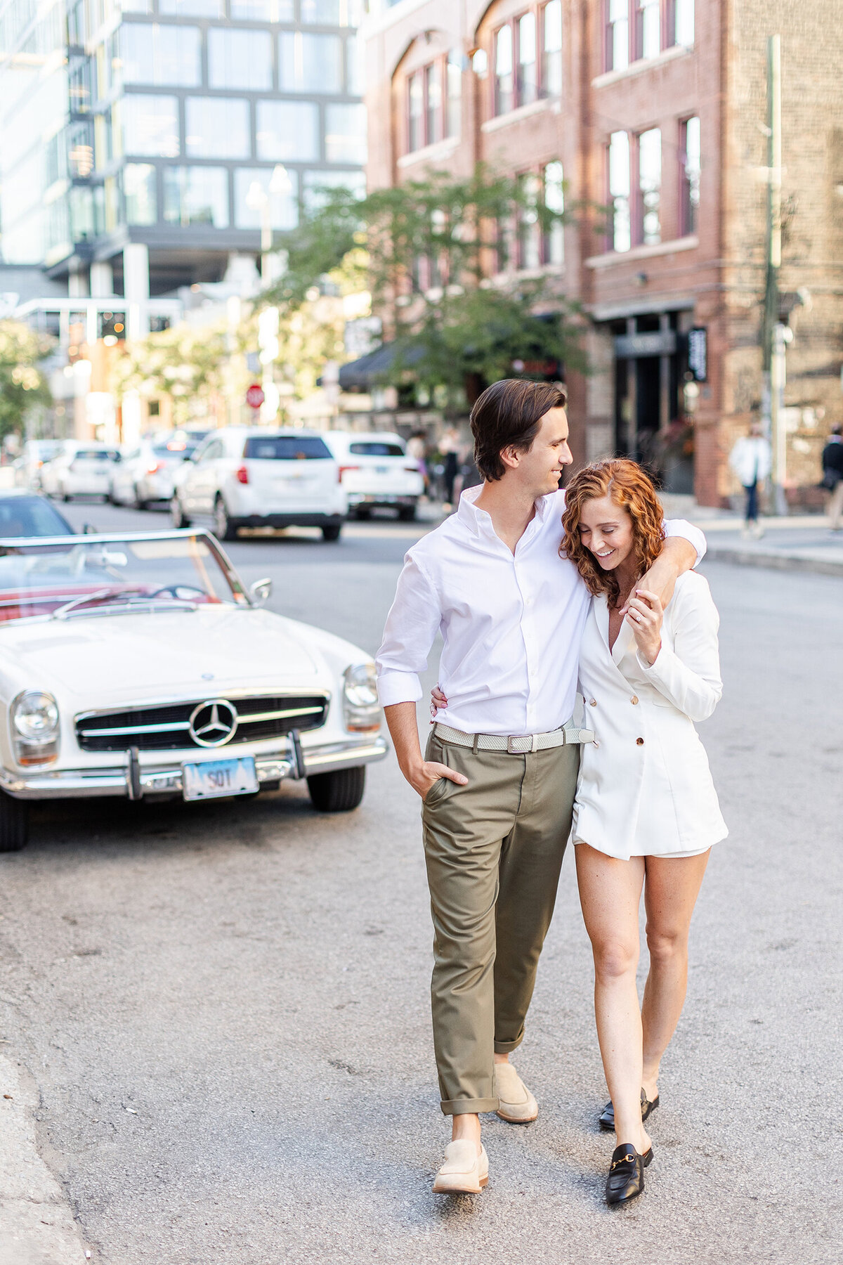 Couple walking arm-in-arm on a city street with a vintage car in the background