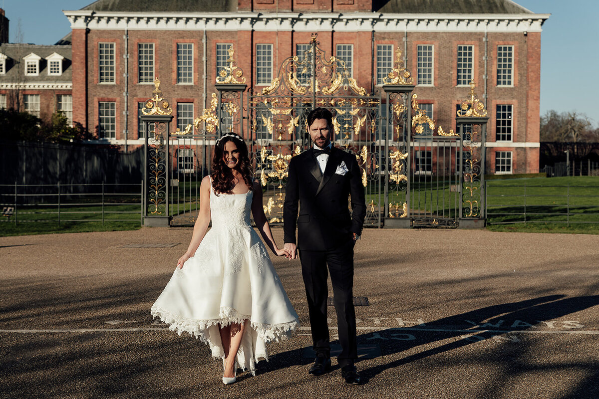 Bride and Groom walk through Kensington holding hands. The Bride in a Josephine Scott dress, the groom in a tuxedo and bow tie.