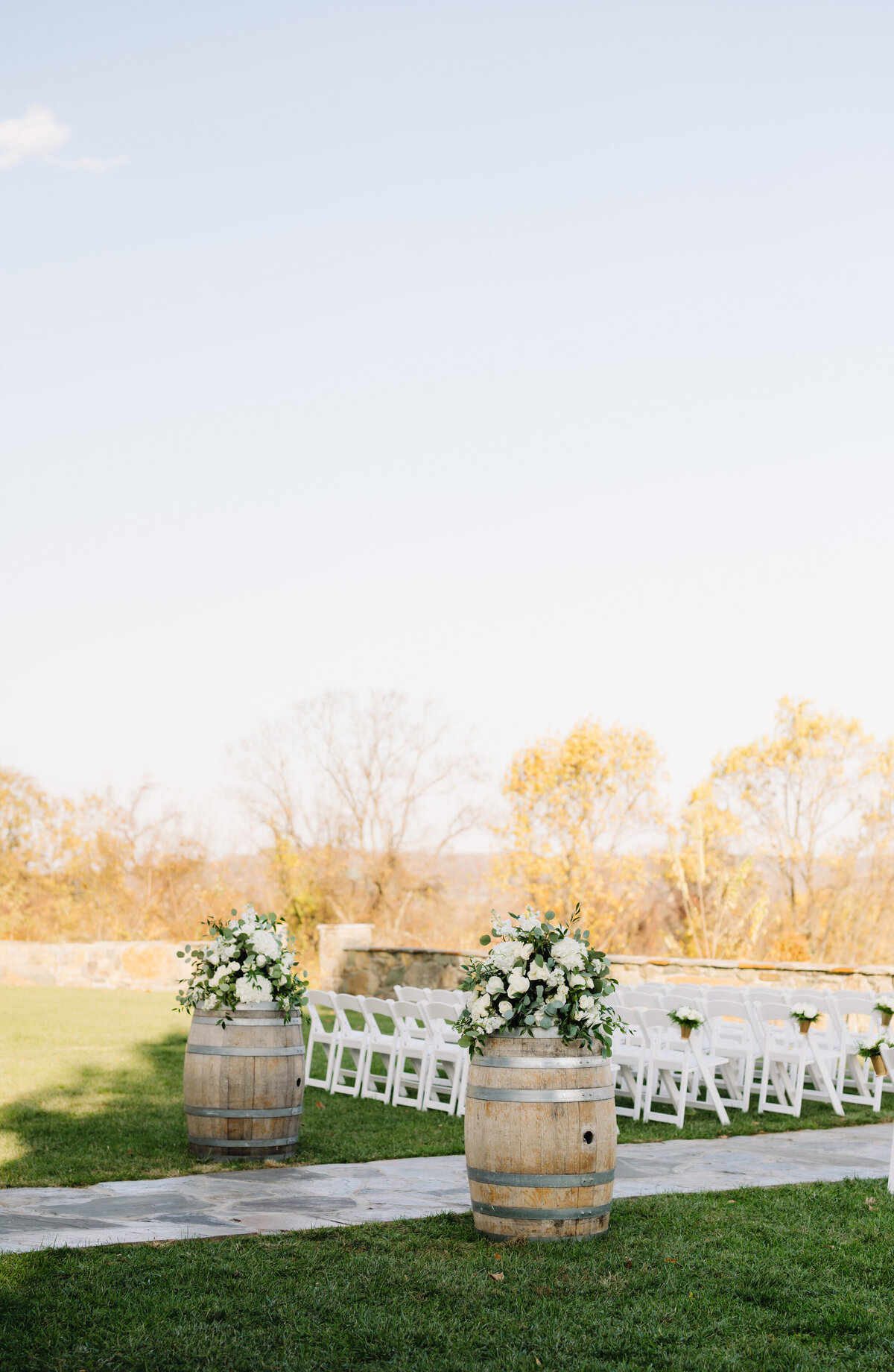 outdoor ceremony decor at Charlottesville wedding venues outdoor ceremony space with white chairs, white roses and treeline in the distance