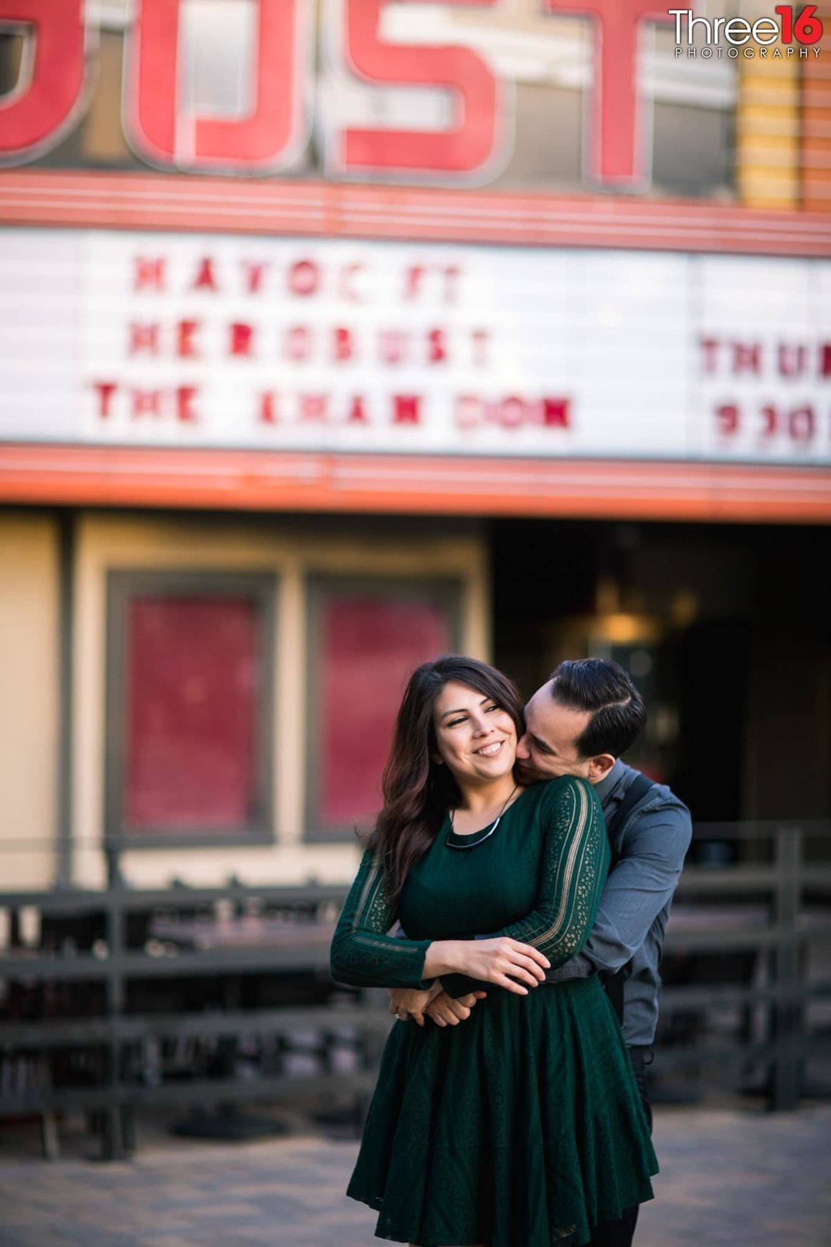 Groom to be hugs his Bride from behind and whispers in her ear at the Yost Theater