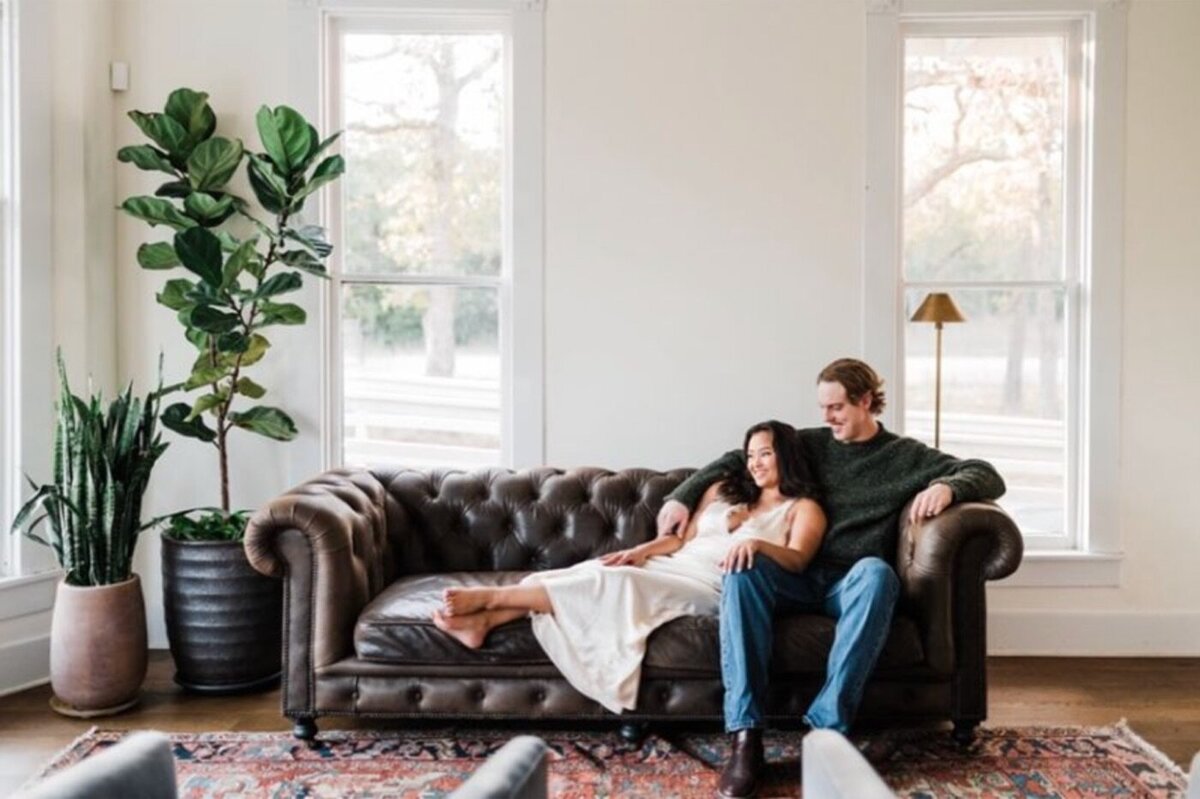 Engaged couple relaxing on a leather sofa in the mansion's sunlit living room