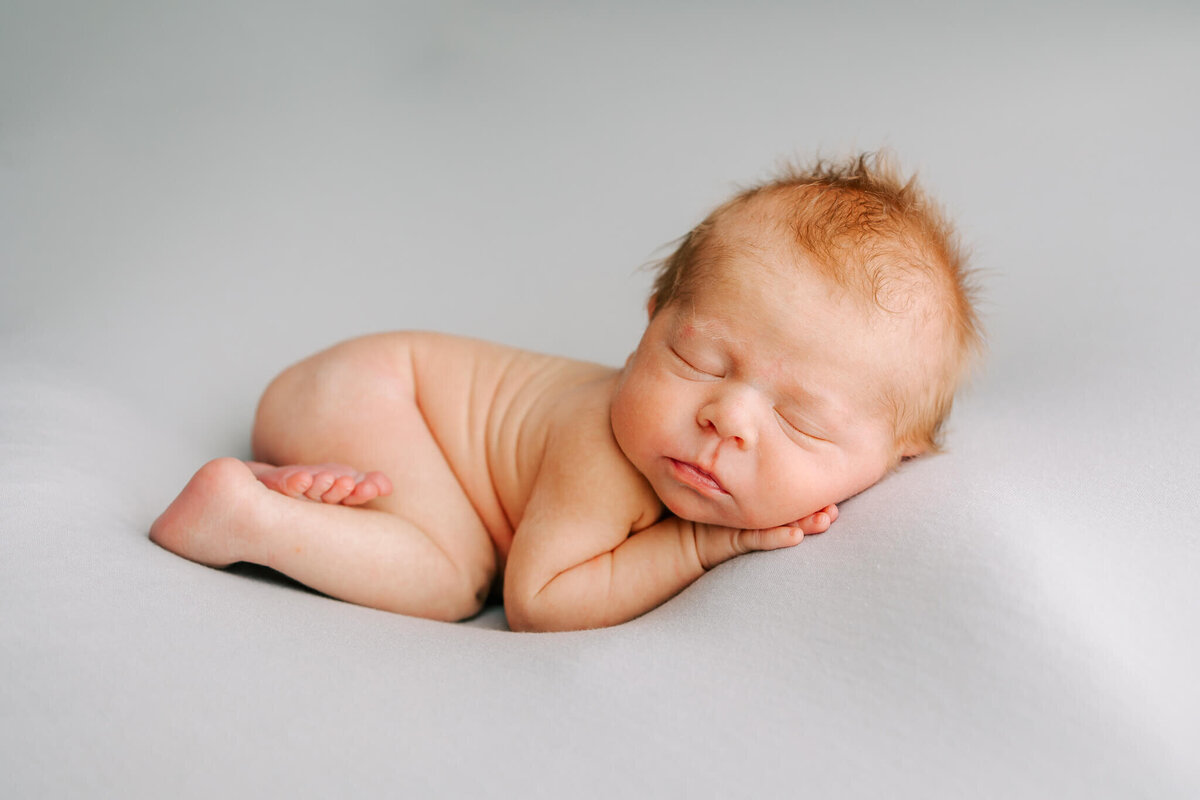 portrait of newborn boy with red hair sleeping on blue blanket.