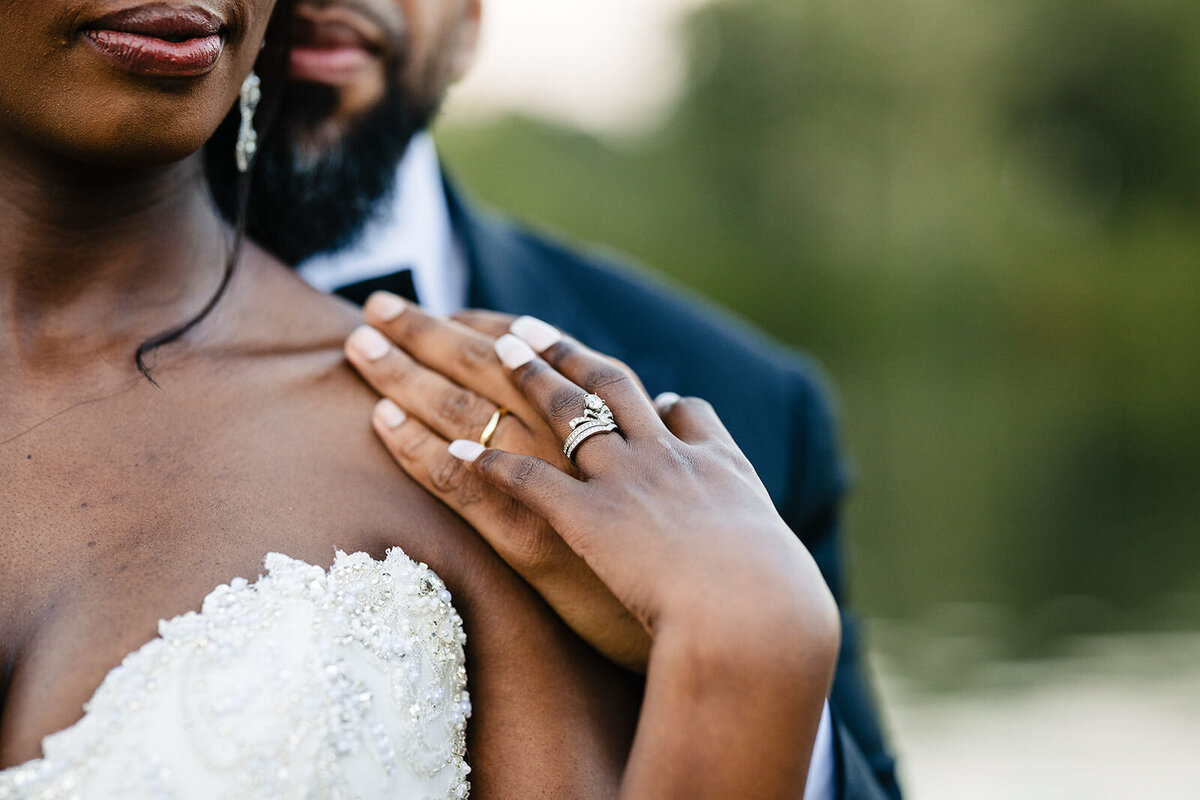 Close-up of a bride and groom, focusing on their hands and wedding rings, with the bride's bouquet in the foreground