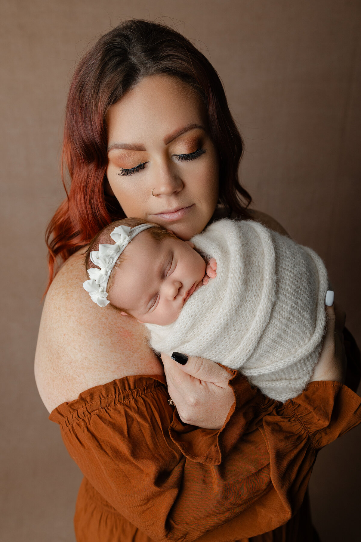 Mother holding her swaddled newborn daughter close, styled in a cream wrap and lace headband during their studio session. Captured by Inland Empire newborn photographer Kaitlyn Dawn Photography.