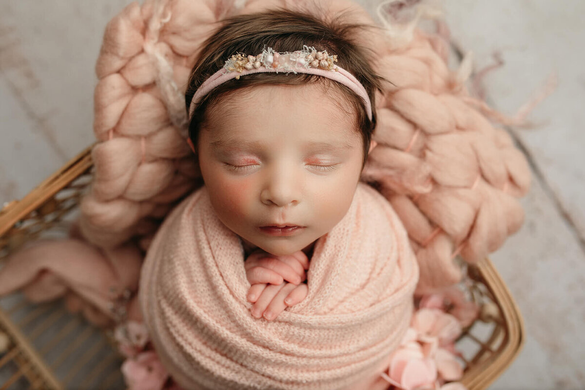 close up shot of newborn sleeping in a pink basket