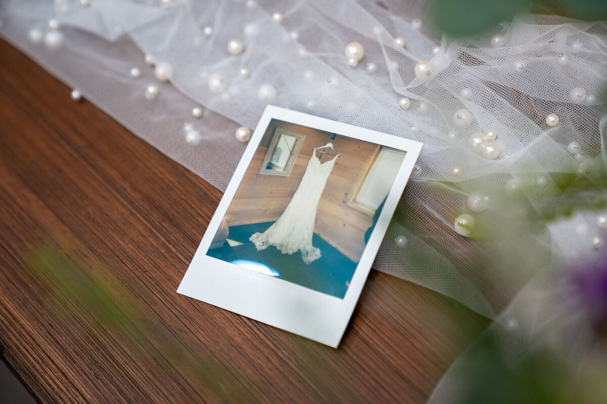 Polaroid photo of a wedding dress on a wooden table with lace and pearls