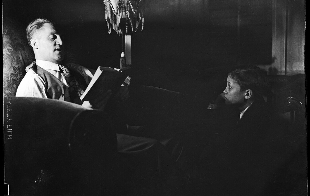 Photograph of an old man reading ab book to a child.