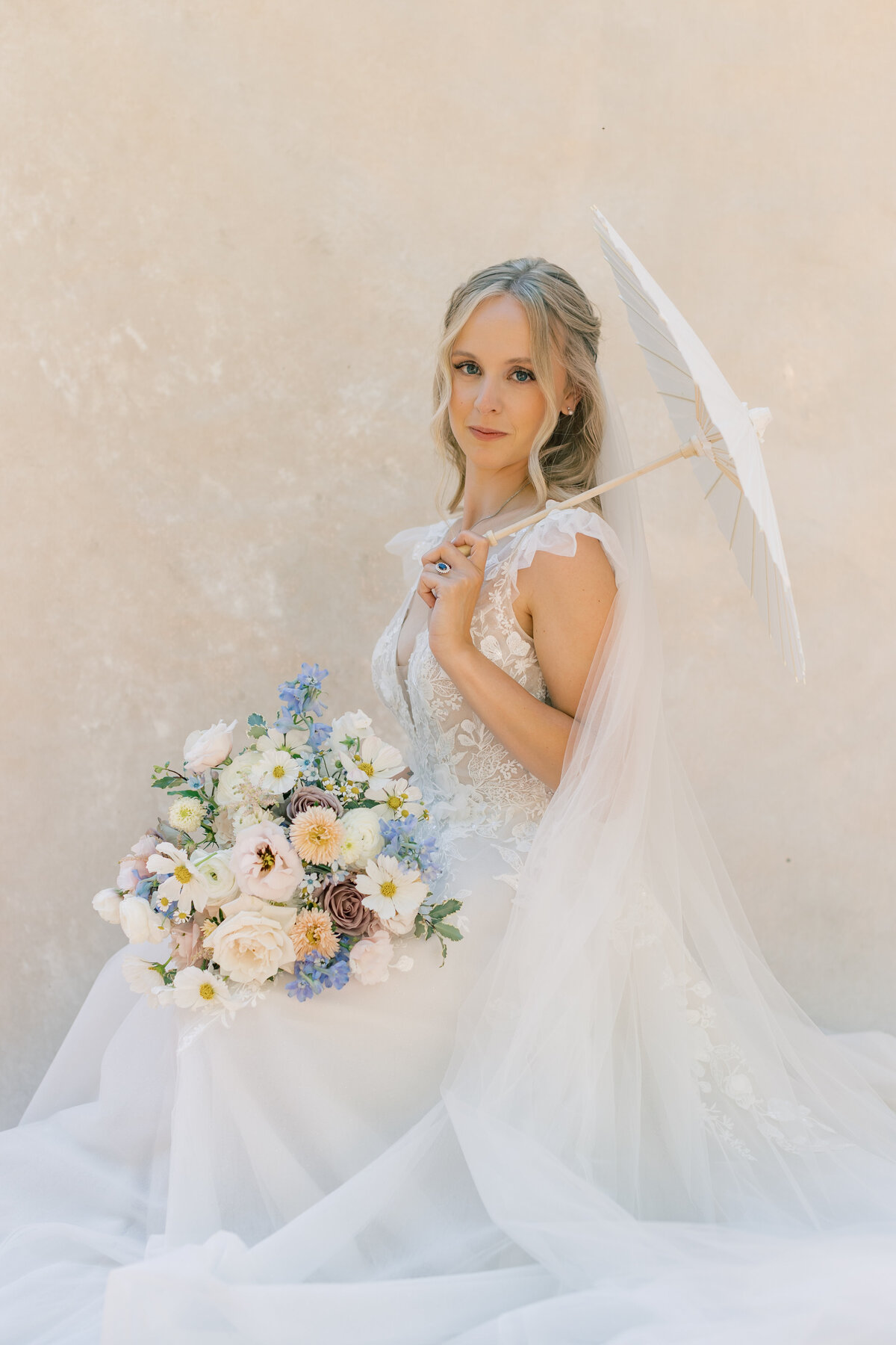 Bride with parasol and flowers in front of canvas backdrop