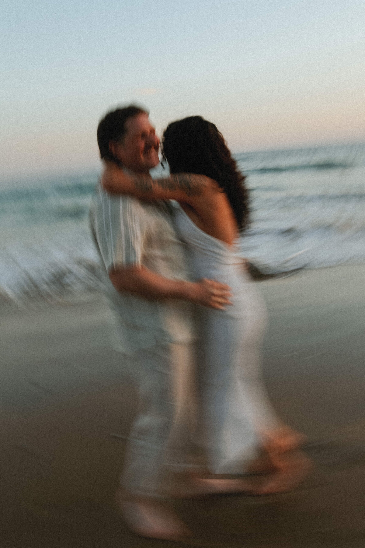 couple standing in front of beach waves swaying back and forth image is slightly blurry