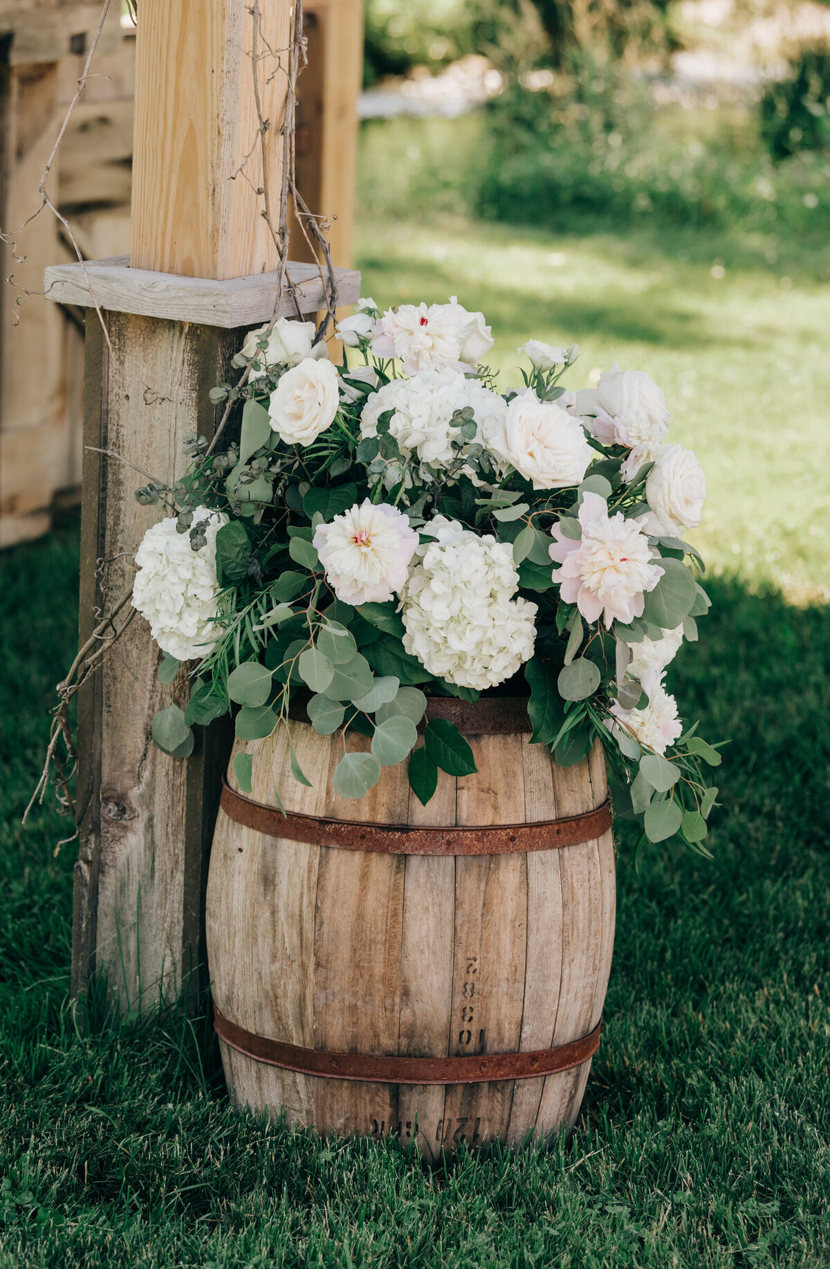 Elegant white florals and eucalyptus on decorative barrel at outdoor wedding ceremony
