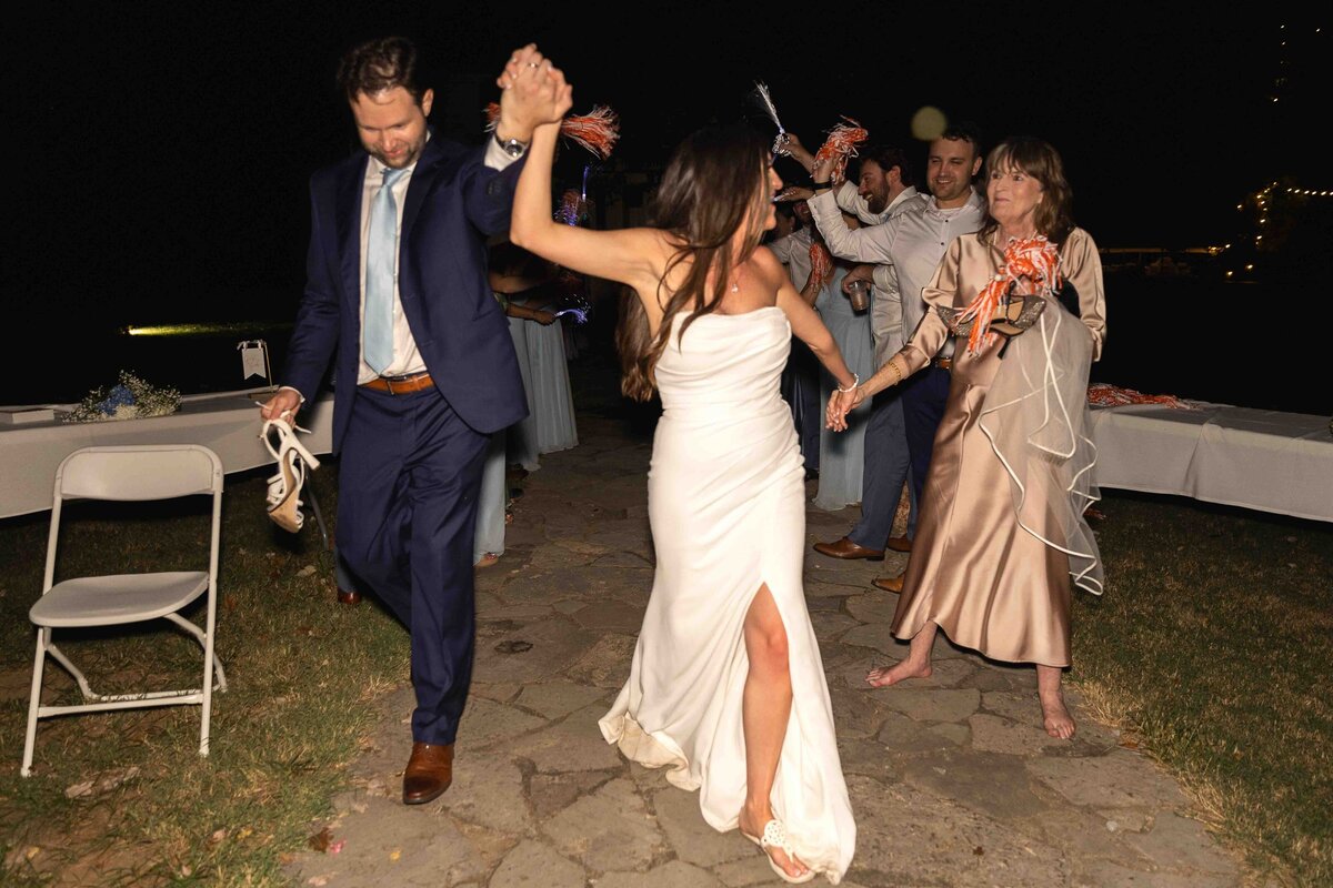 Bride and groom holding hands leaving wedding reception while bride says goodbye to mom