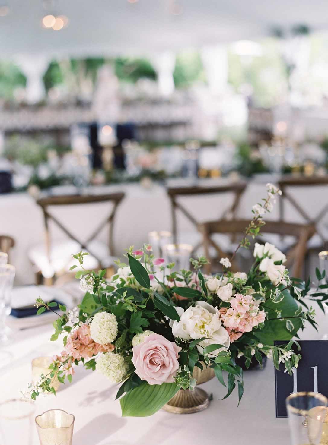 centerpiece of blush roses, white roses, ranunculus, and greenery in gold compote