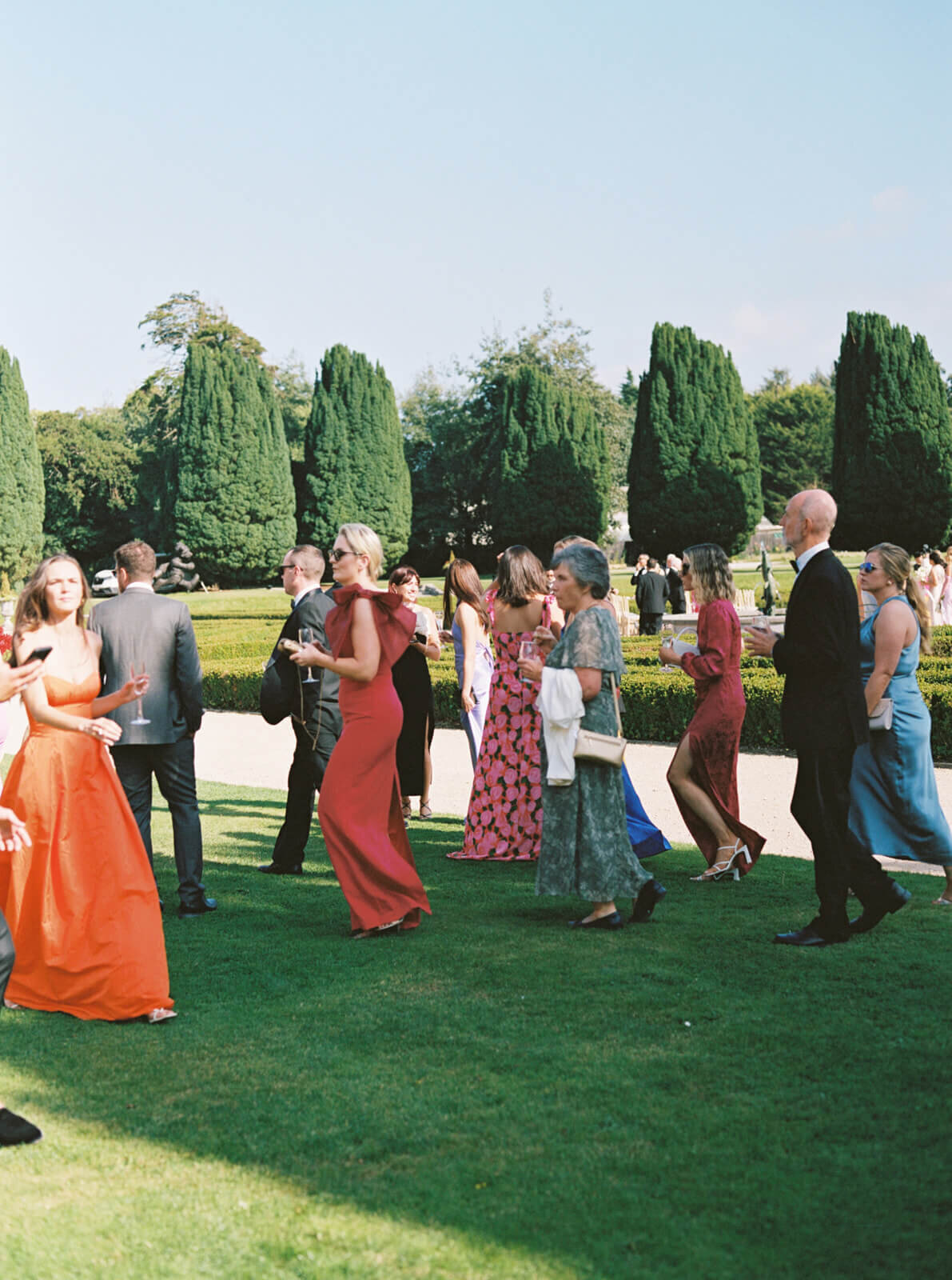 candid image showing wedding guests in colorful dress and suits heading to the gardens for the wedding ceremony