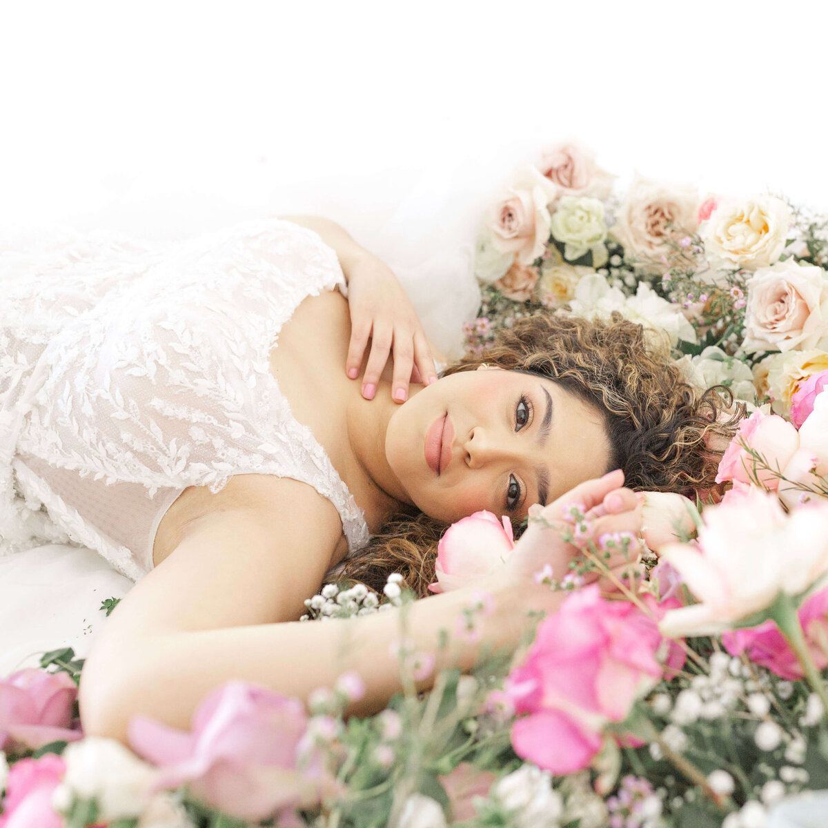 bride lying down surrounded by roses in pink, blush and cream