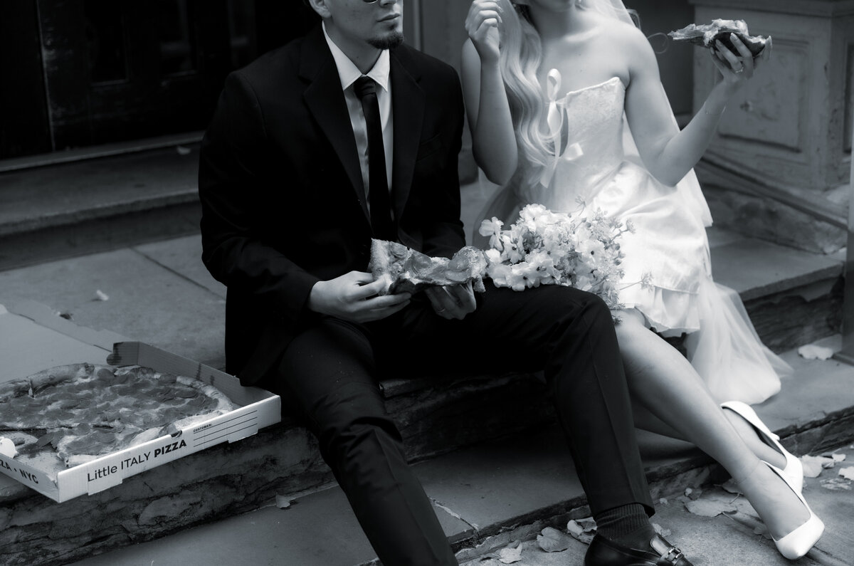Bride and groom sharing a romantic moment while splitting a slice of pizza in NYC.