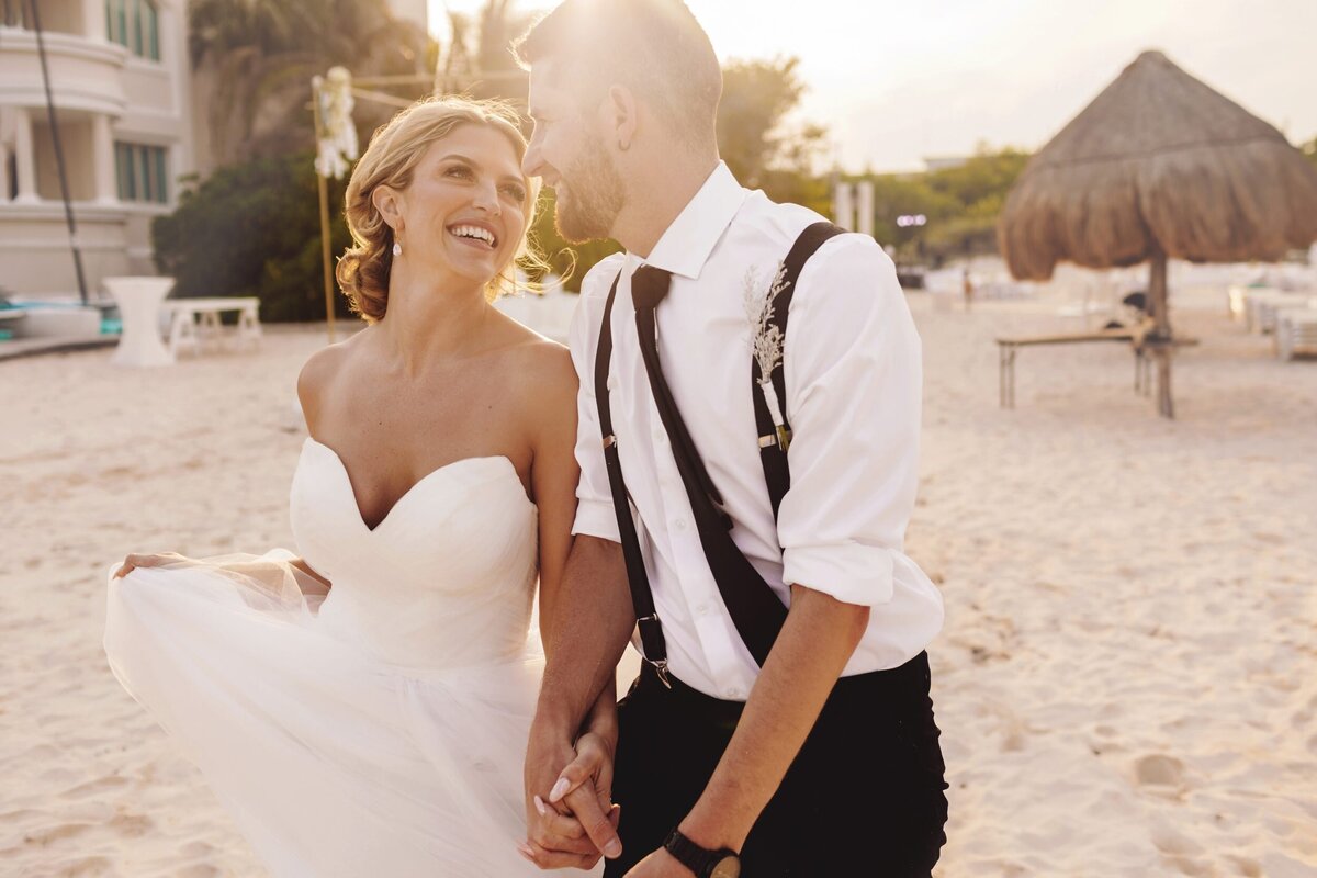 Bride and groom laughing, holding hands and walking on beach in Riviera Maya