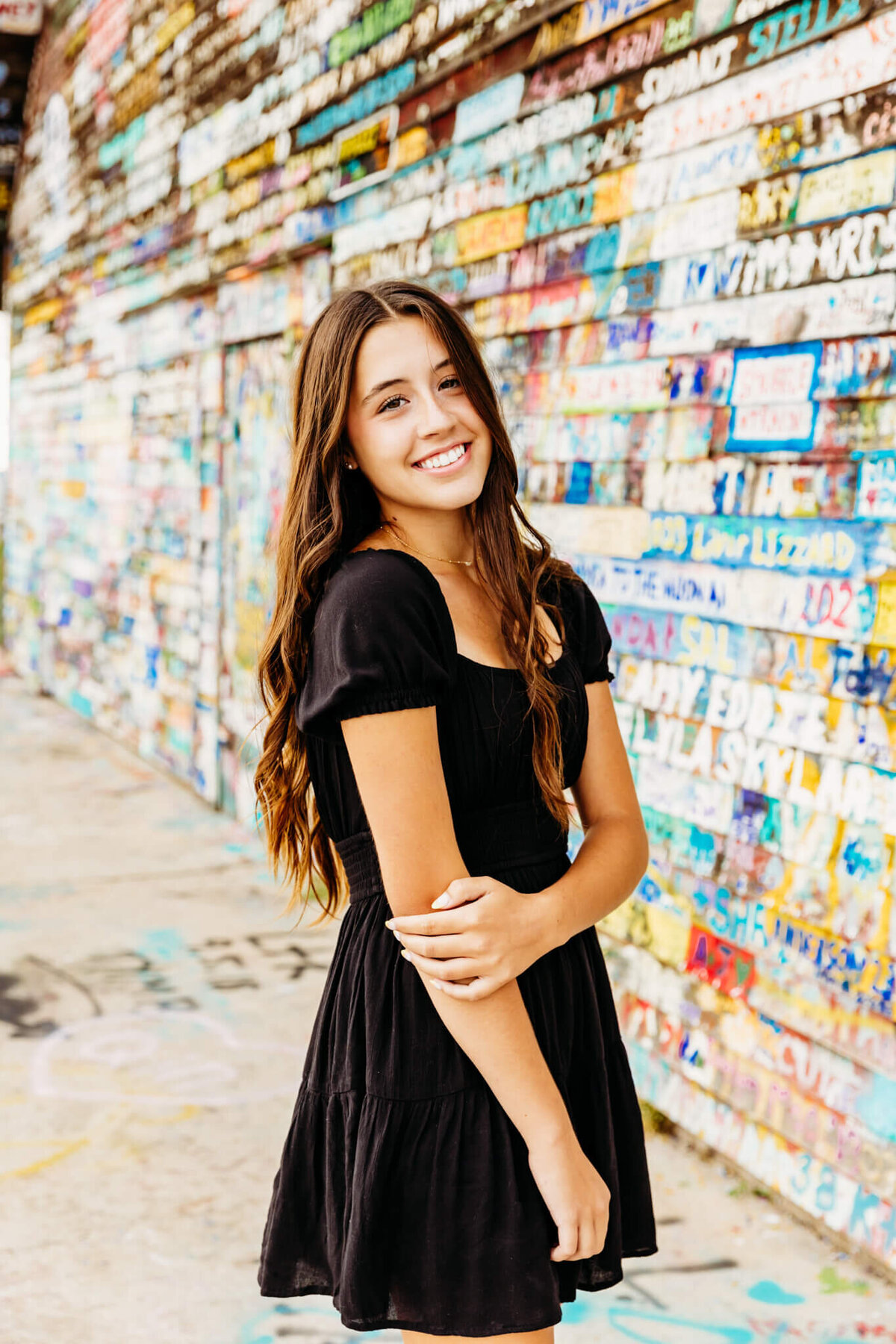 beautiful teen girl in a black dress holding her elbow as she smiles during her Appleton senior photography session