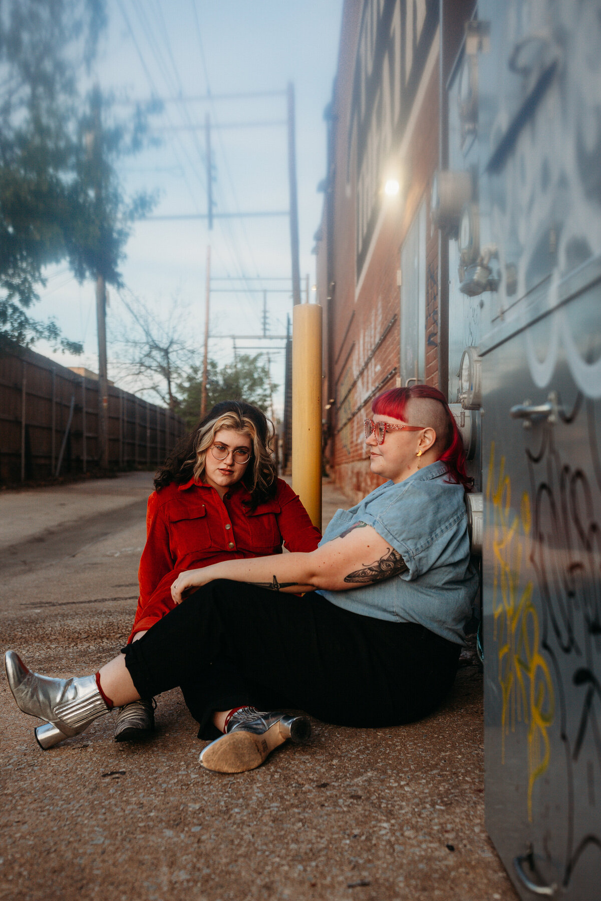 Two individuals seated against an urban backdrop with graffiti, conveying a relaxed and cool demeanor in their casual wear