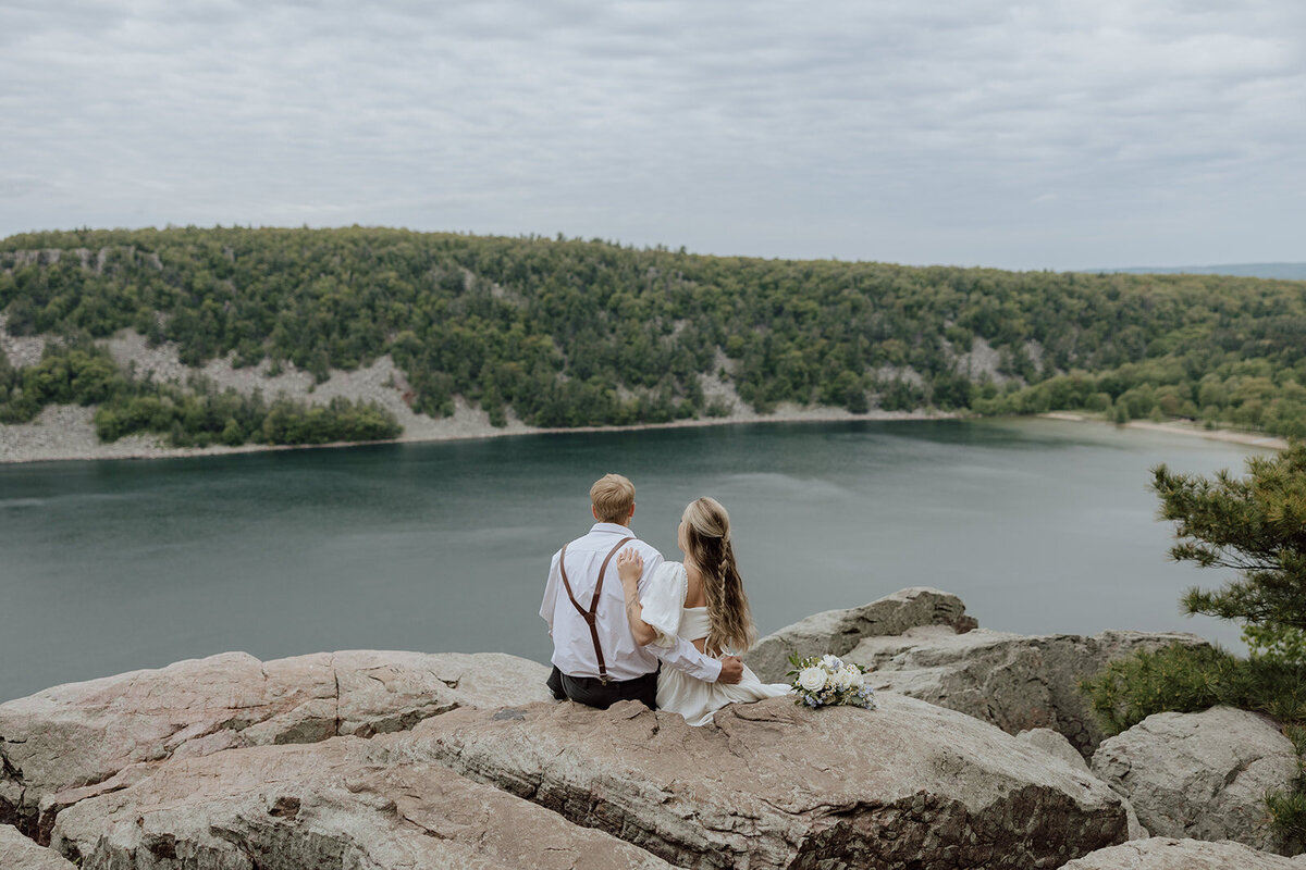 elopement at devils lake state park. Photo of a couple sitting on an overlook looking out at the view.