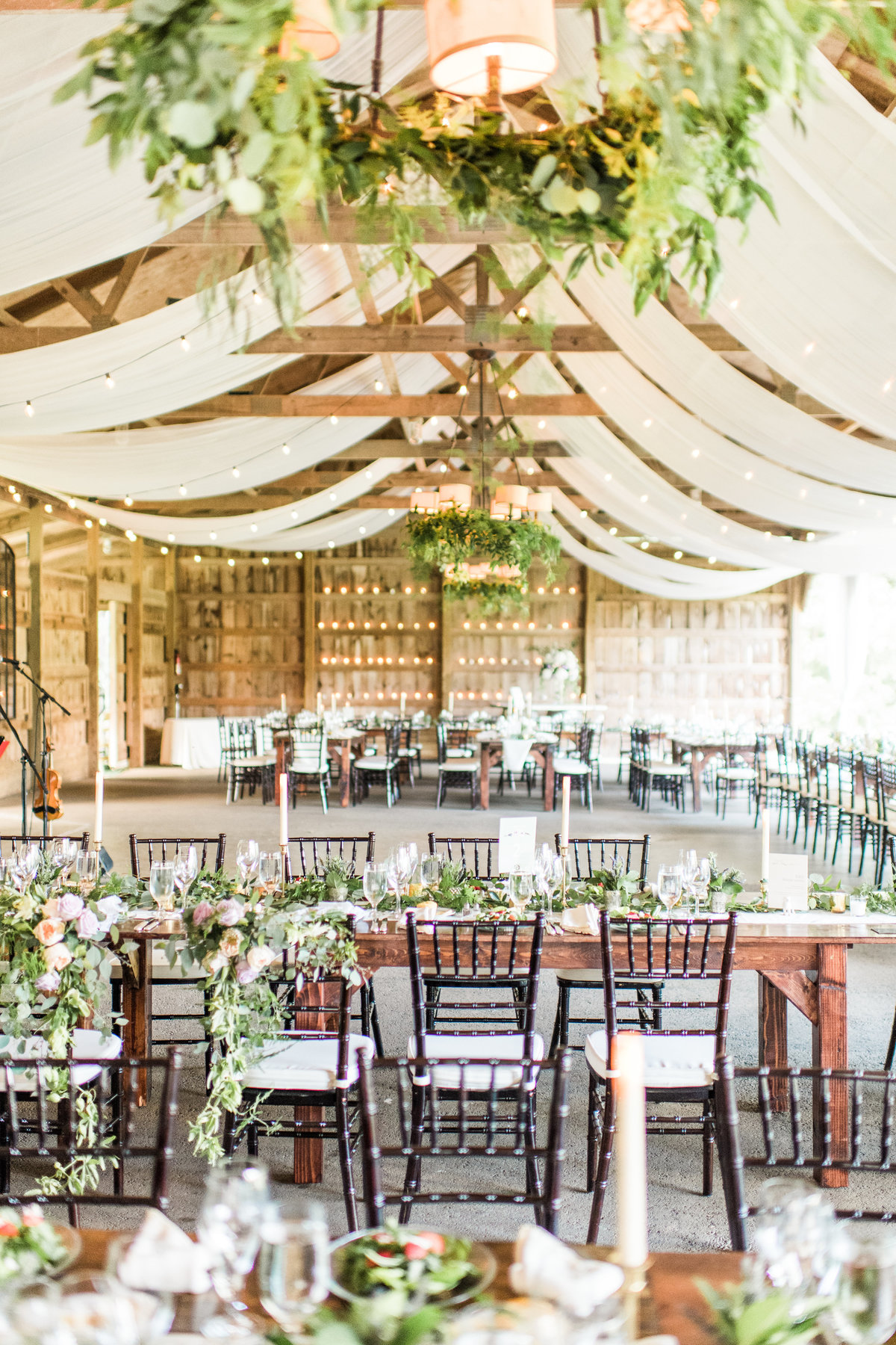 Elegant reception space decorated with hanging cloth, greenery and florals lining the tables.