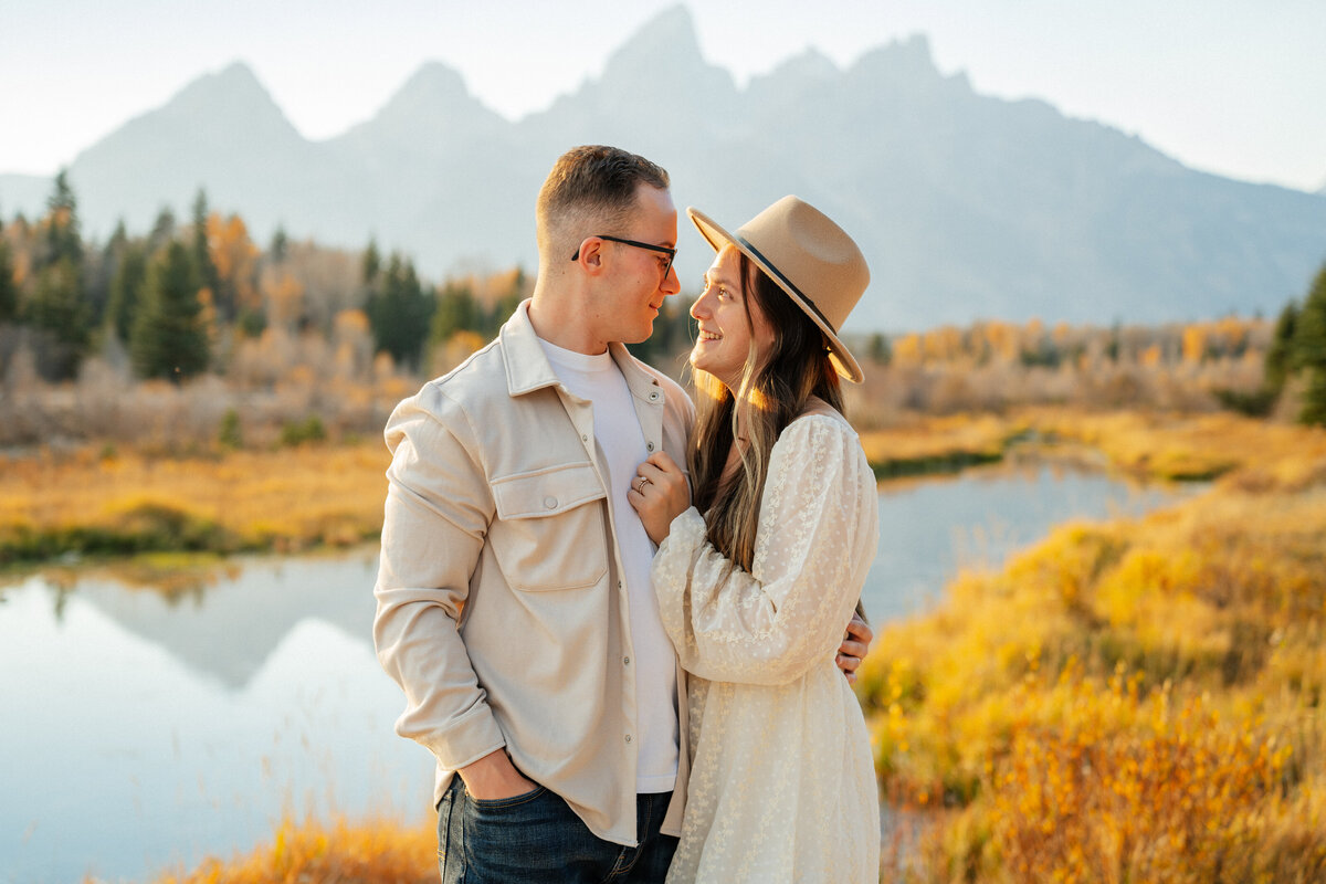 Couples photography in Grand Teton National park during fall. A man is holding his fiance with one hand behind her back. She has her hand on his chest and they are looking into each others eyes.