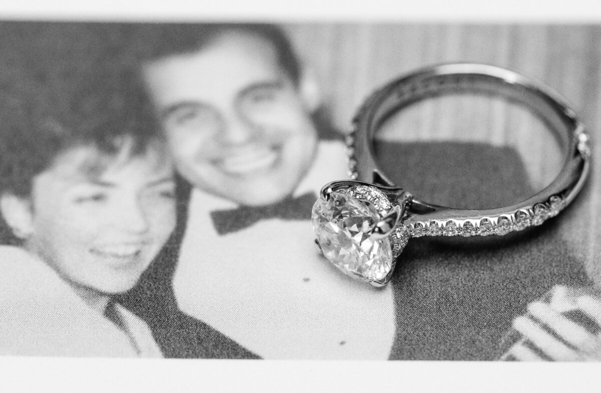 A close-up of a sparkling engagement ring placed over a vintage wedding photo, symbolizing timeless love. A sentimental wedding detail that beautifully honors family history and tradition.