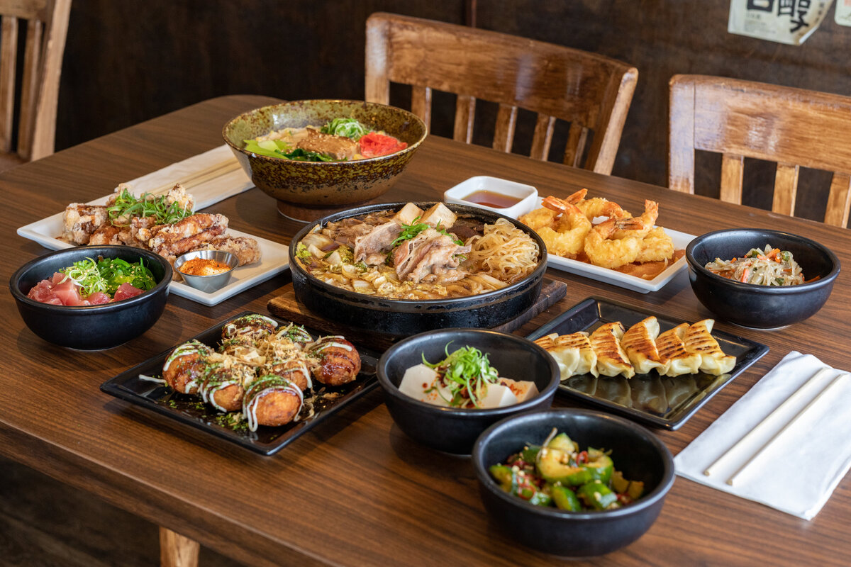 A table full of traditional japanese food including pork ramen, pho, shrimp tempura, crab rangoons, and other appetizers.