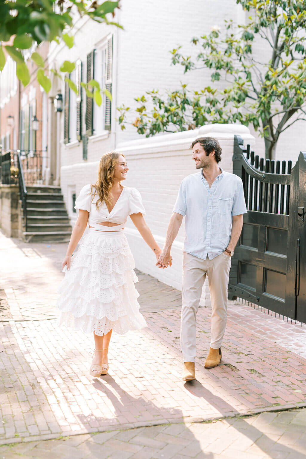 Fun image of couple looking at each other, smiling and walking hand in hand while they take engagement photos taken by Rachael Mattio