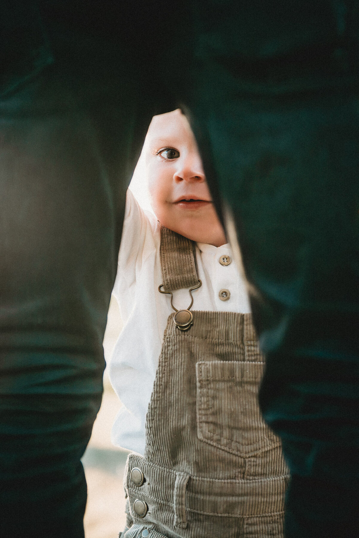 a boy looking through the legs of his dad during a family photoshoot captured by Bie