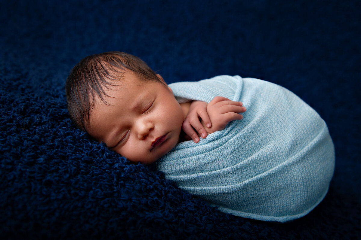 baby on a blue backdrop wrapped in a light blue newborn wrap