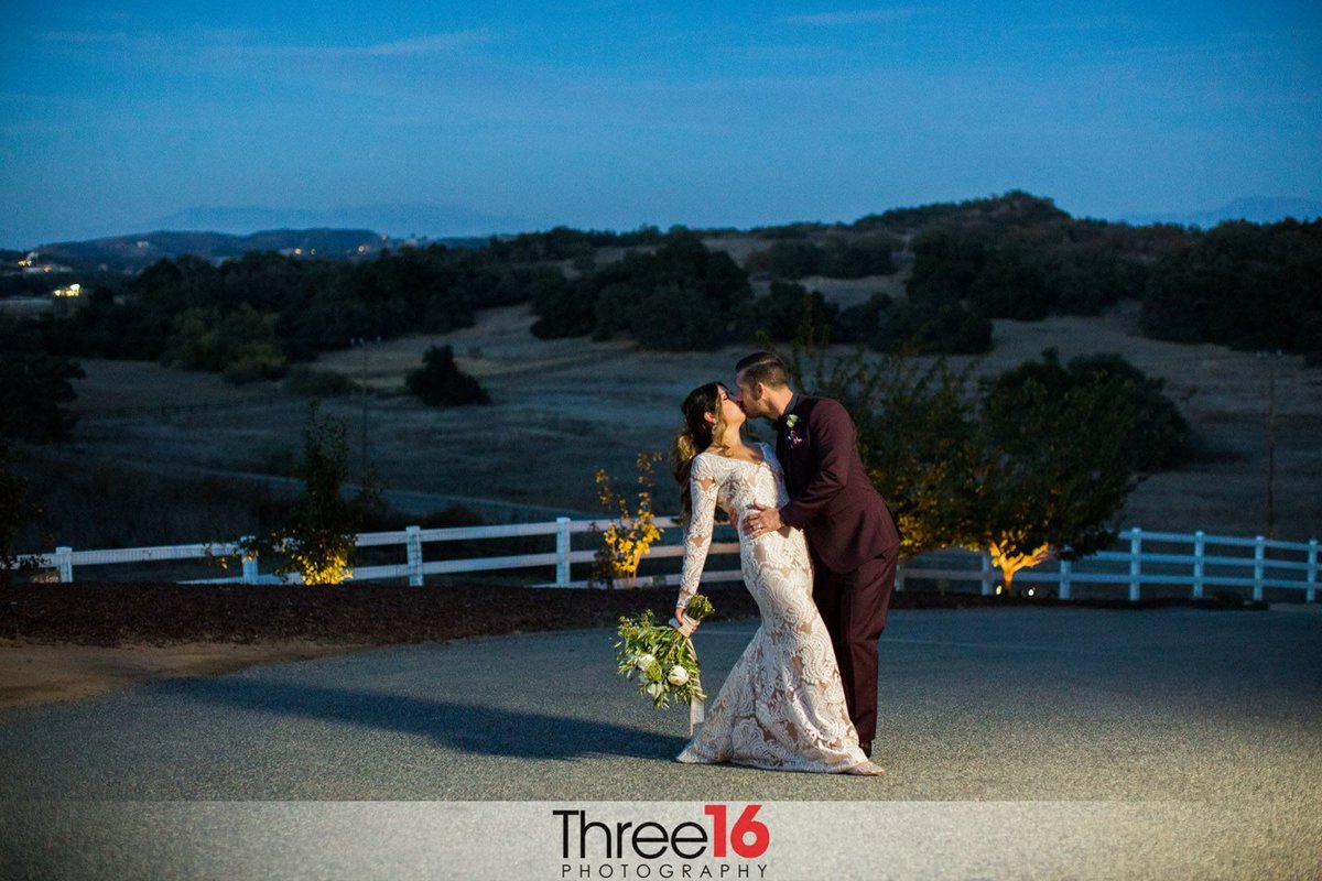 Groom dips and kisses his Bride during an evening photoshoot with the spotlight on them