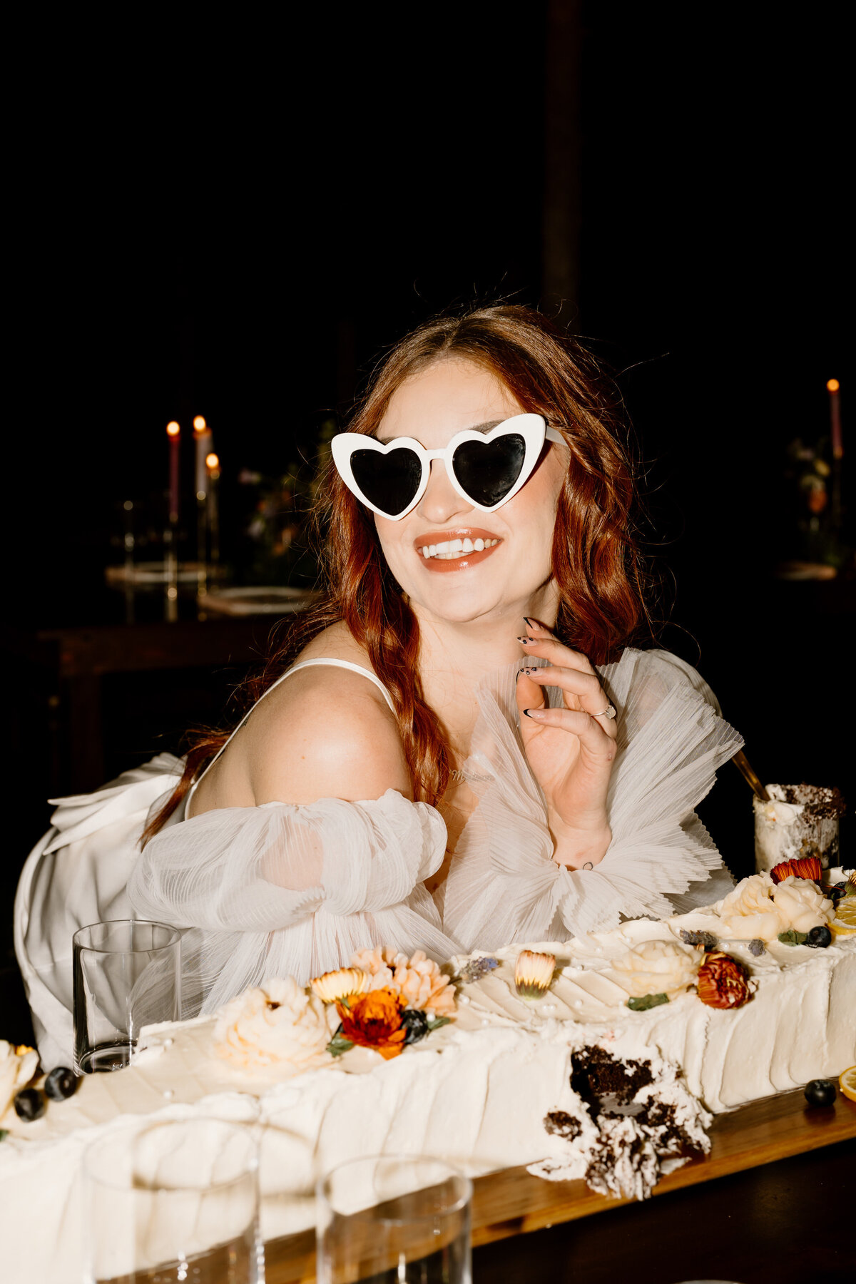 Bride wearing sunglasses sitting by cake