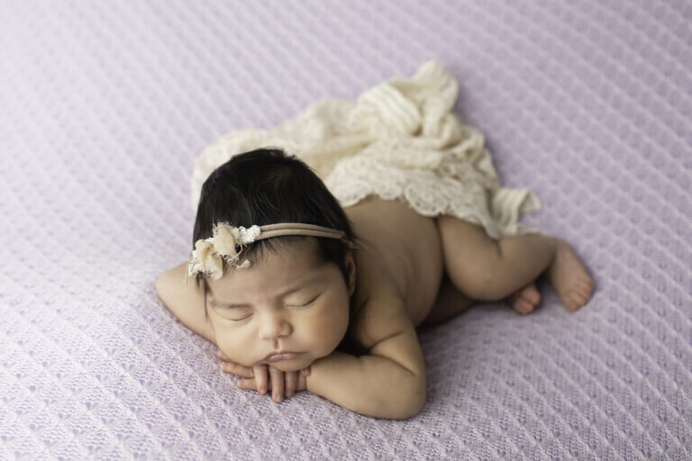 Newborn baby girl peacefully lying on her stomach, with her tiny hands tucked under her chin, creating a soft and serene portrait
