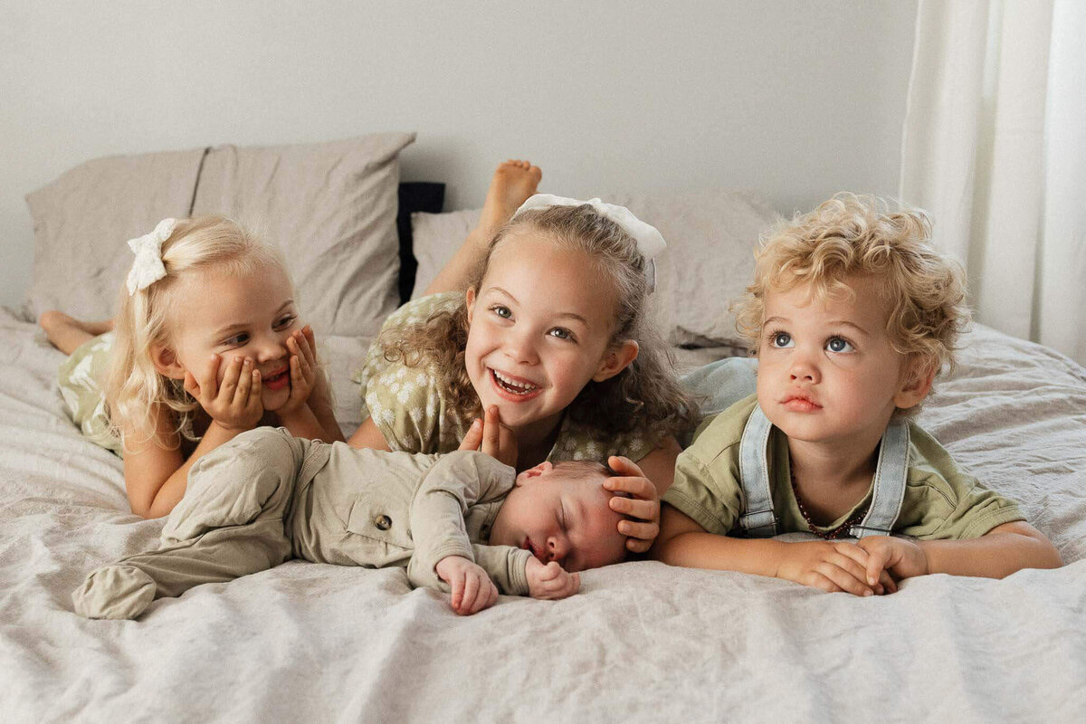 Older siblings admire their newborn brother on a bed during a relaxed lifestyle photography session in Cleveland.