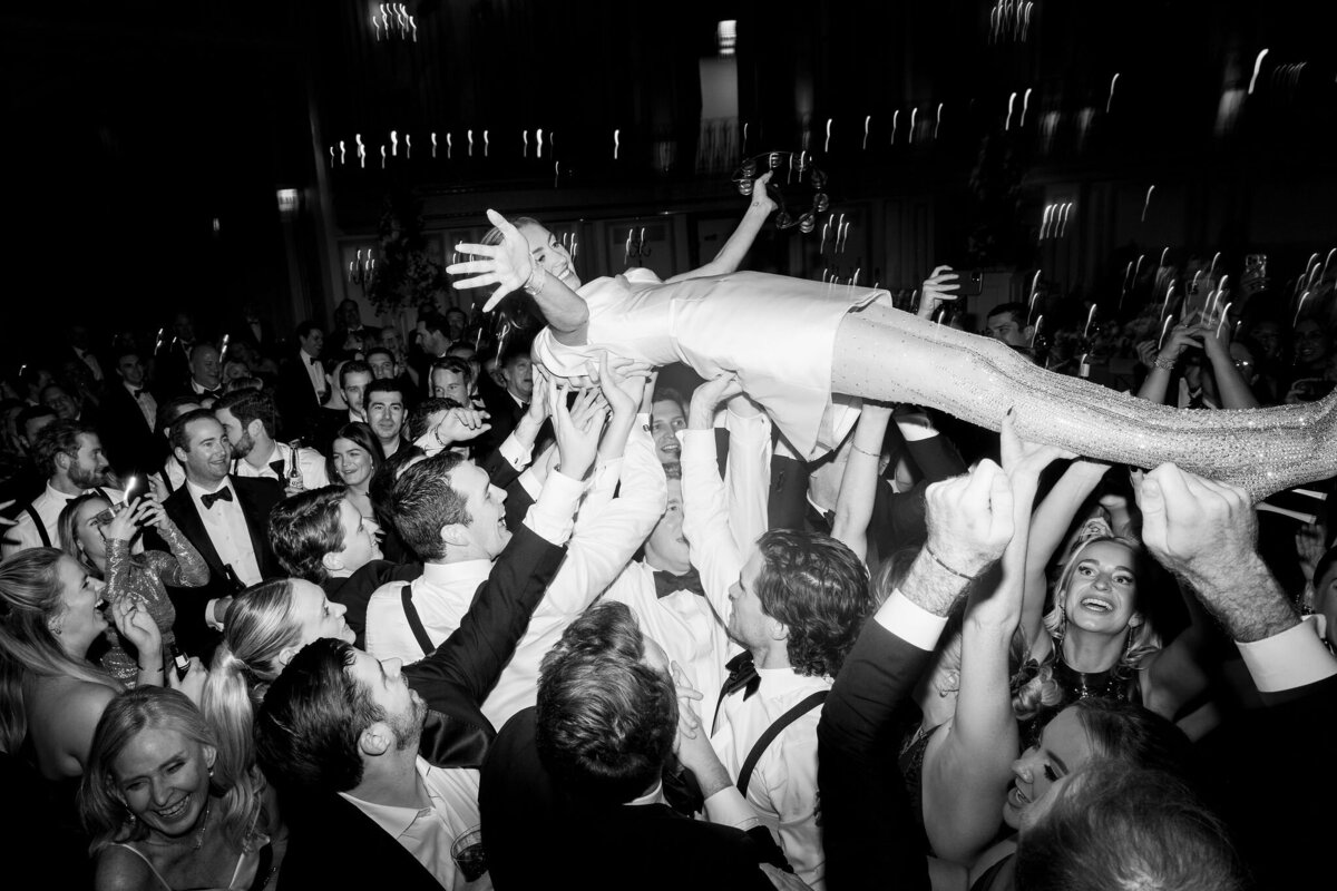 Black and white photo of a wedding guest crowd-surfing during a lively reception party.